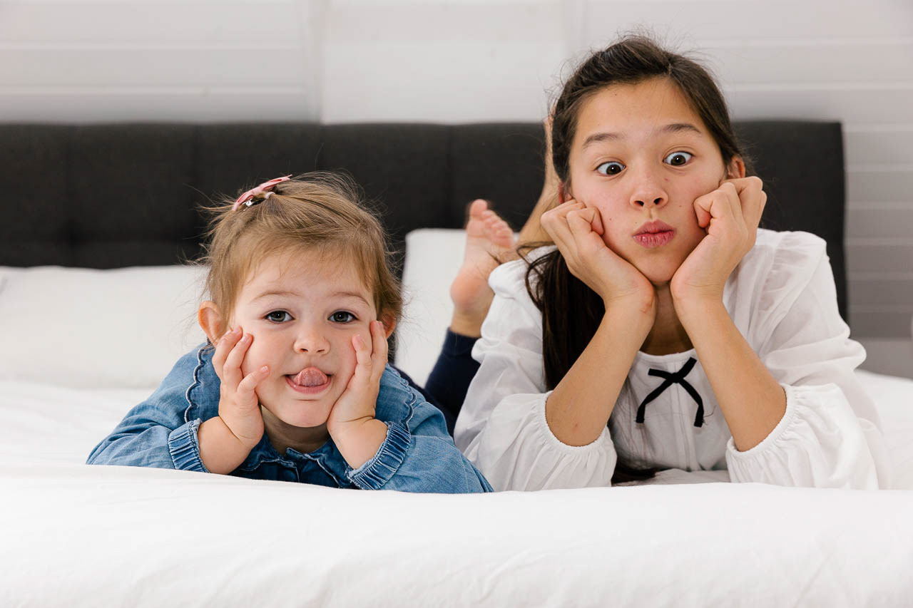 Die Schwestern ziehen Grimassen und zeigen ihre verspielte Seite – ein Moment, der Kinderlachen einfängt.
