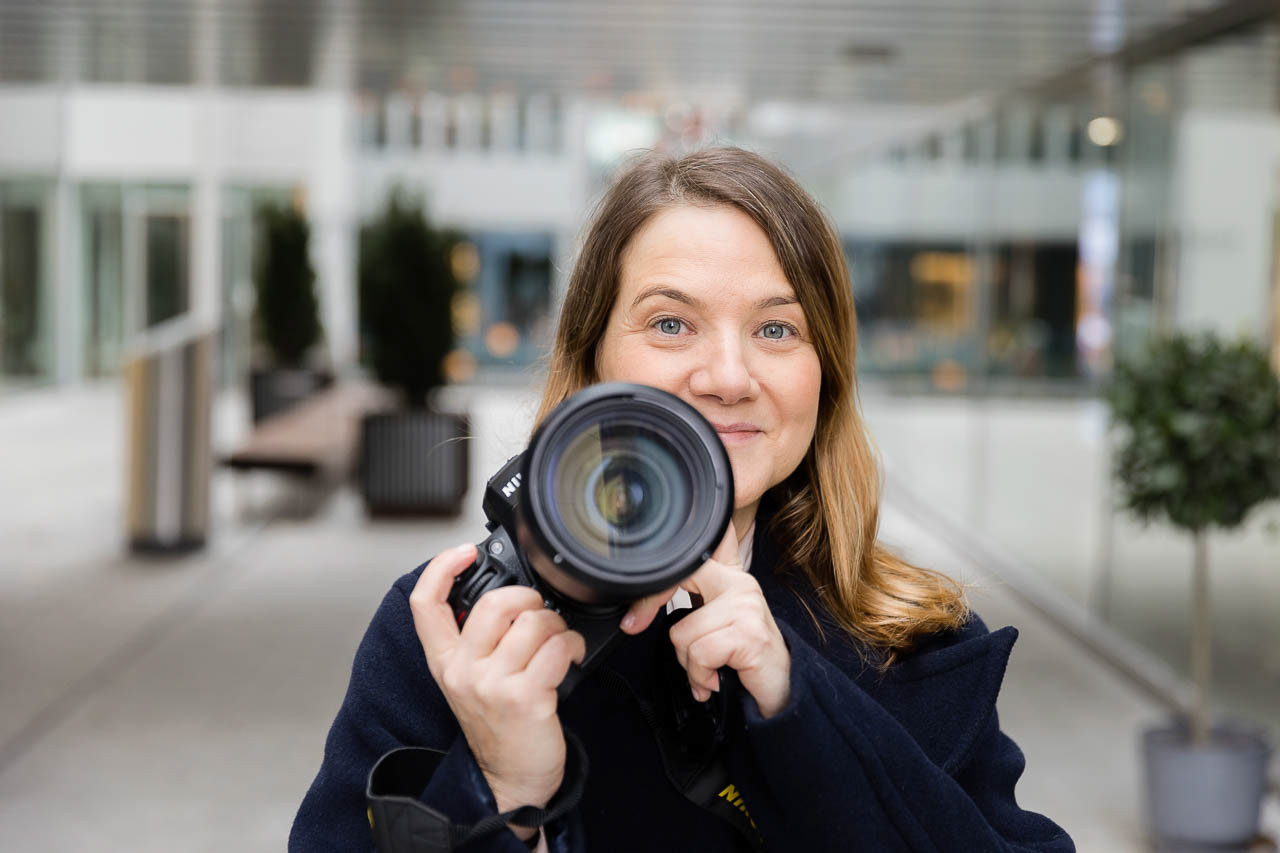 Porträt einer Fotografin mit Kamera, aufgenommen in urbaner Umgebung, ideal für kreative Selbstständige.