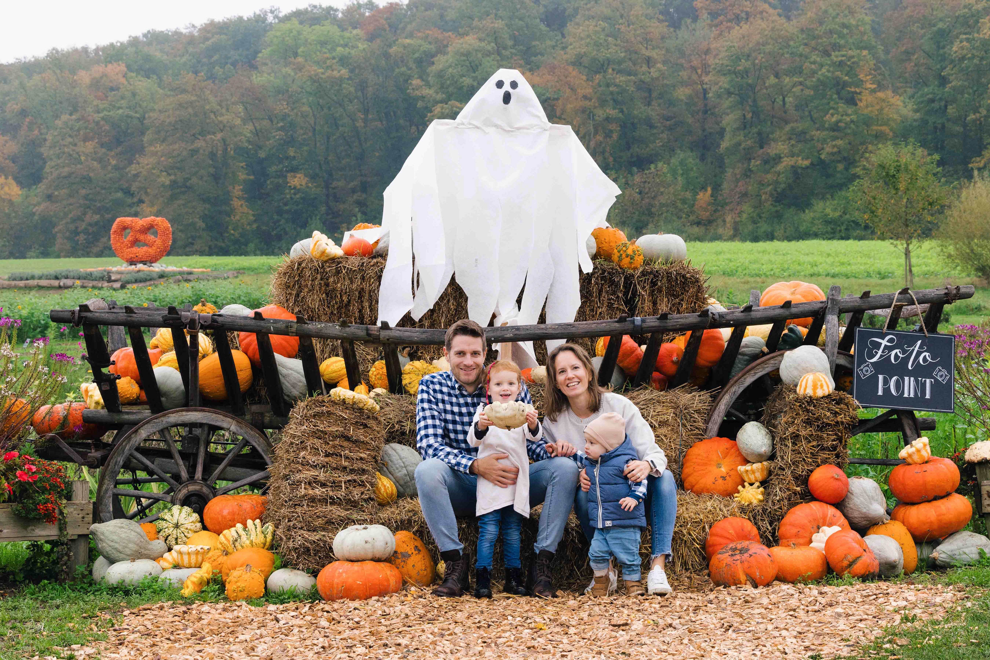 Familienfotografie während Halloween: Ein Familienporträt auf einem Foto-Point mit Heuballen, Kürbissen und einem lustigen Geister-Dekor im Hintergrund