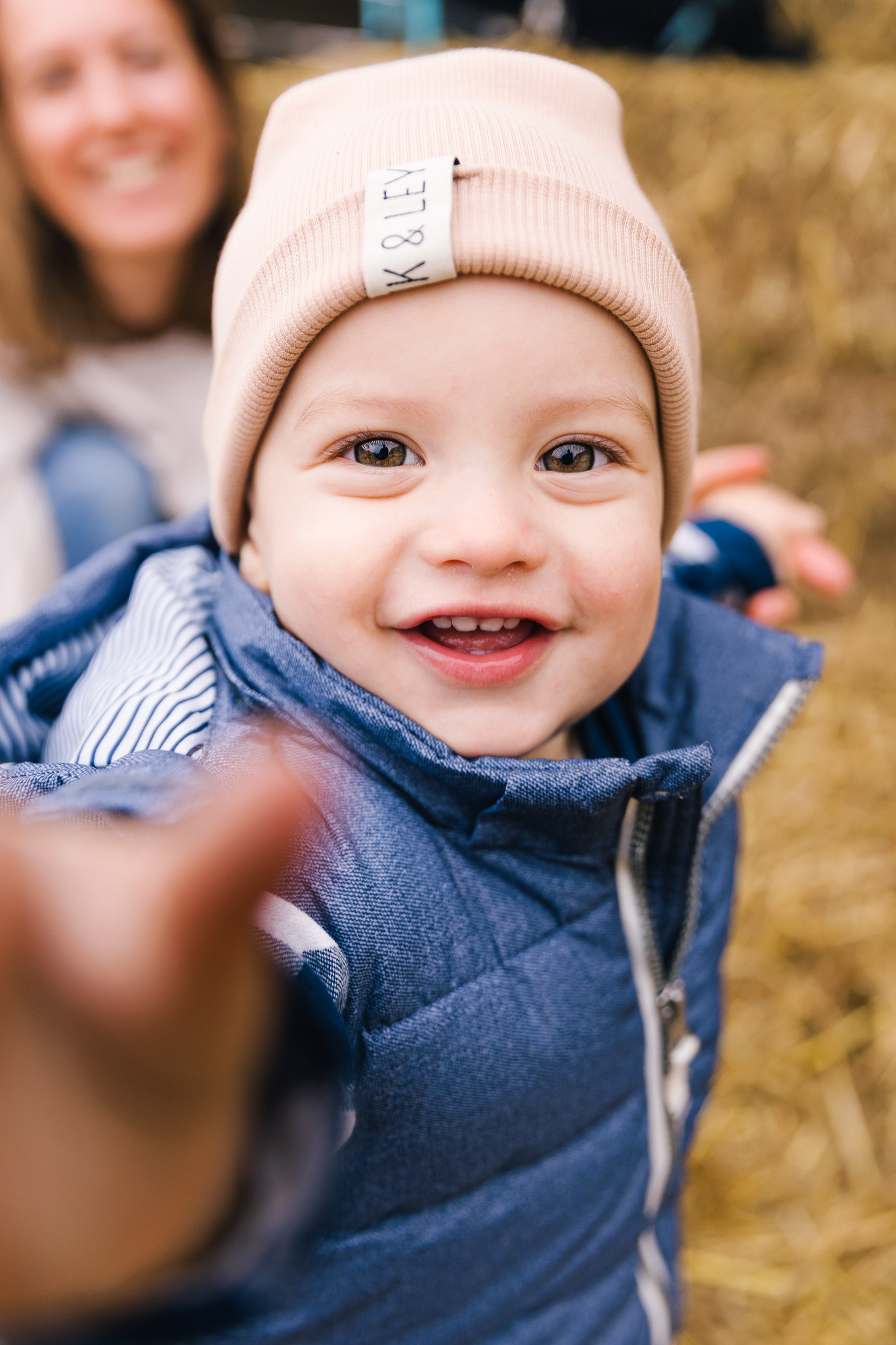 Familienfotografie: Ein fröhliches Baby greift spielerisch in die Kamera während eines Fotoshootings im Herbst.