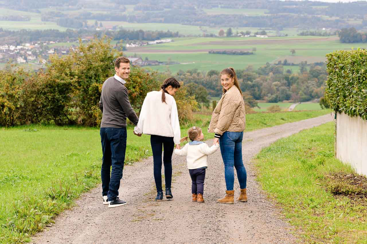 Die Familie spaziert Hand in Hand einen ländlichen Weg entlang, mit einer atemberaubenden Herbstlandschaft im Hintergrund.