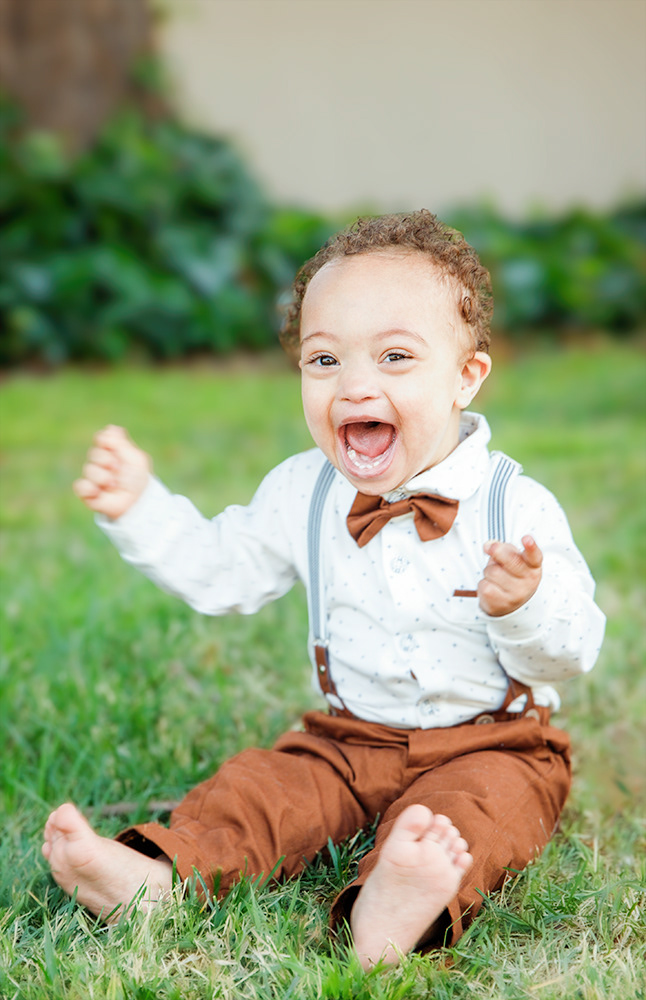 Toddler boy sitting on grass with big smile