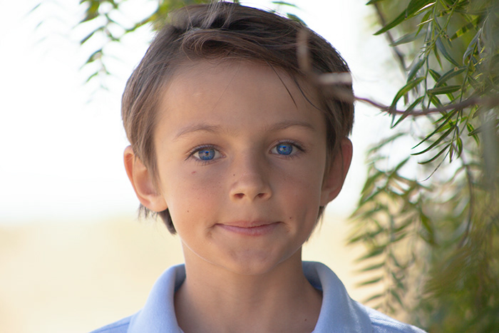 portrait of young blue eye boy standing next to tree