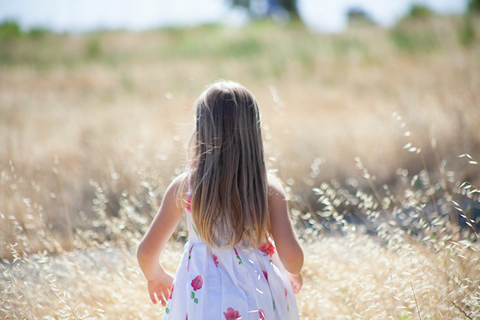 8 year old blond girl with back turned looking at golden wheat field