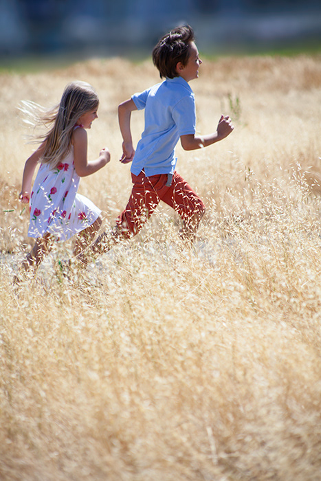 Photography of brother and sister running and playing in golden field