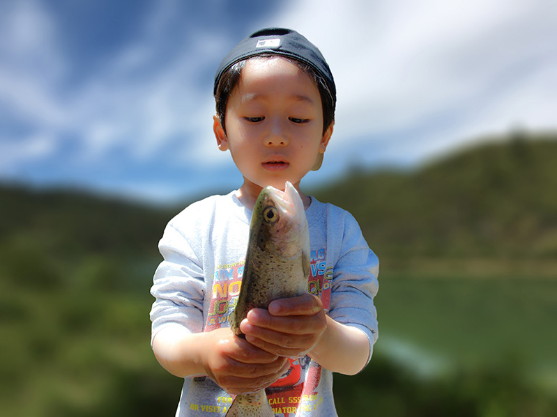 Photography of young boy holding fish wearing baseball cap at lake