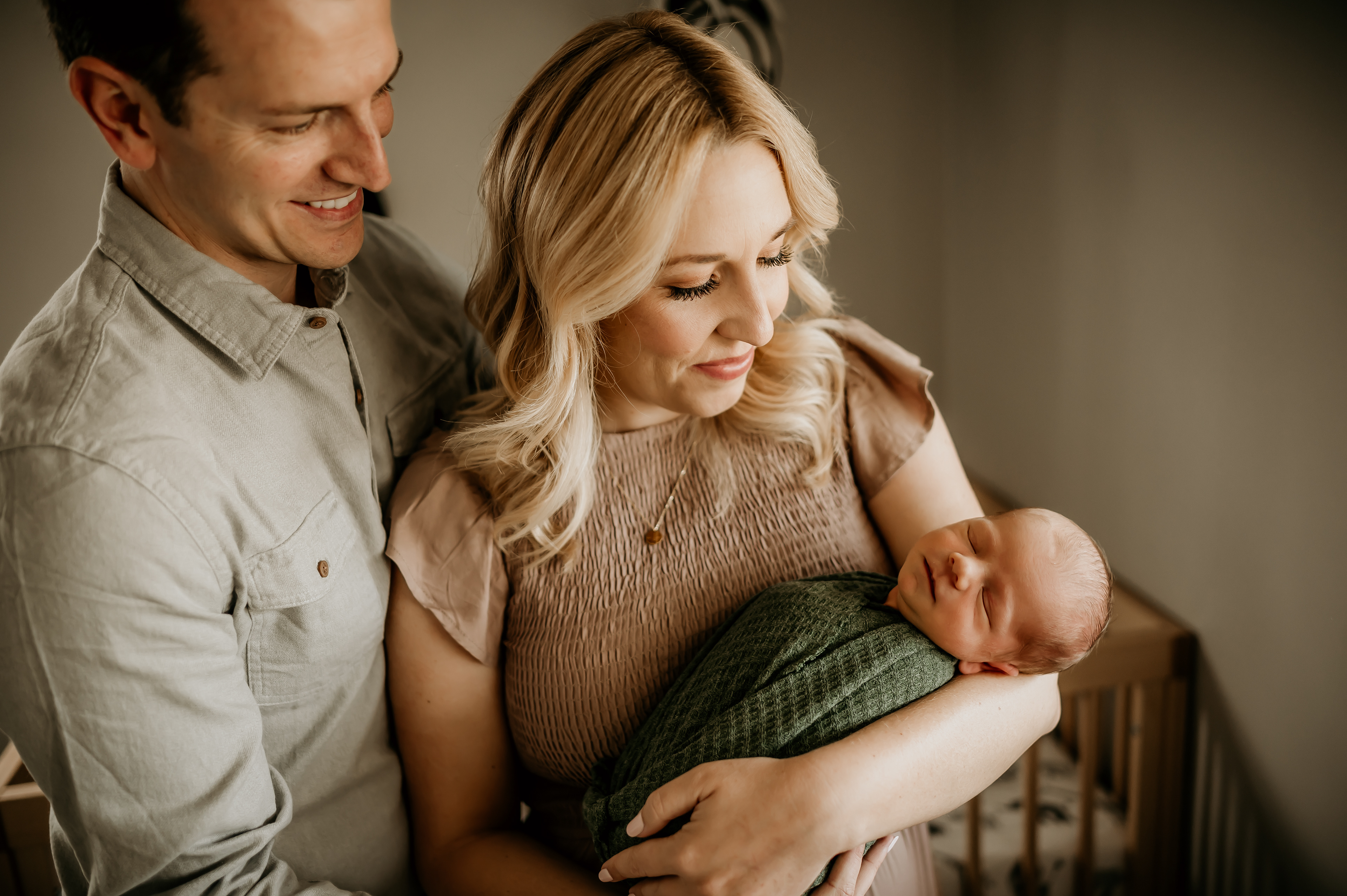 A blond women holding a newborn baby in a green blanket. Photograph taken by Hearts and Arrow Photography at a newborn session in Sacramento, California.