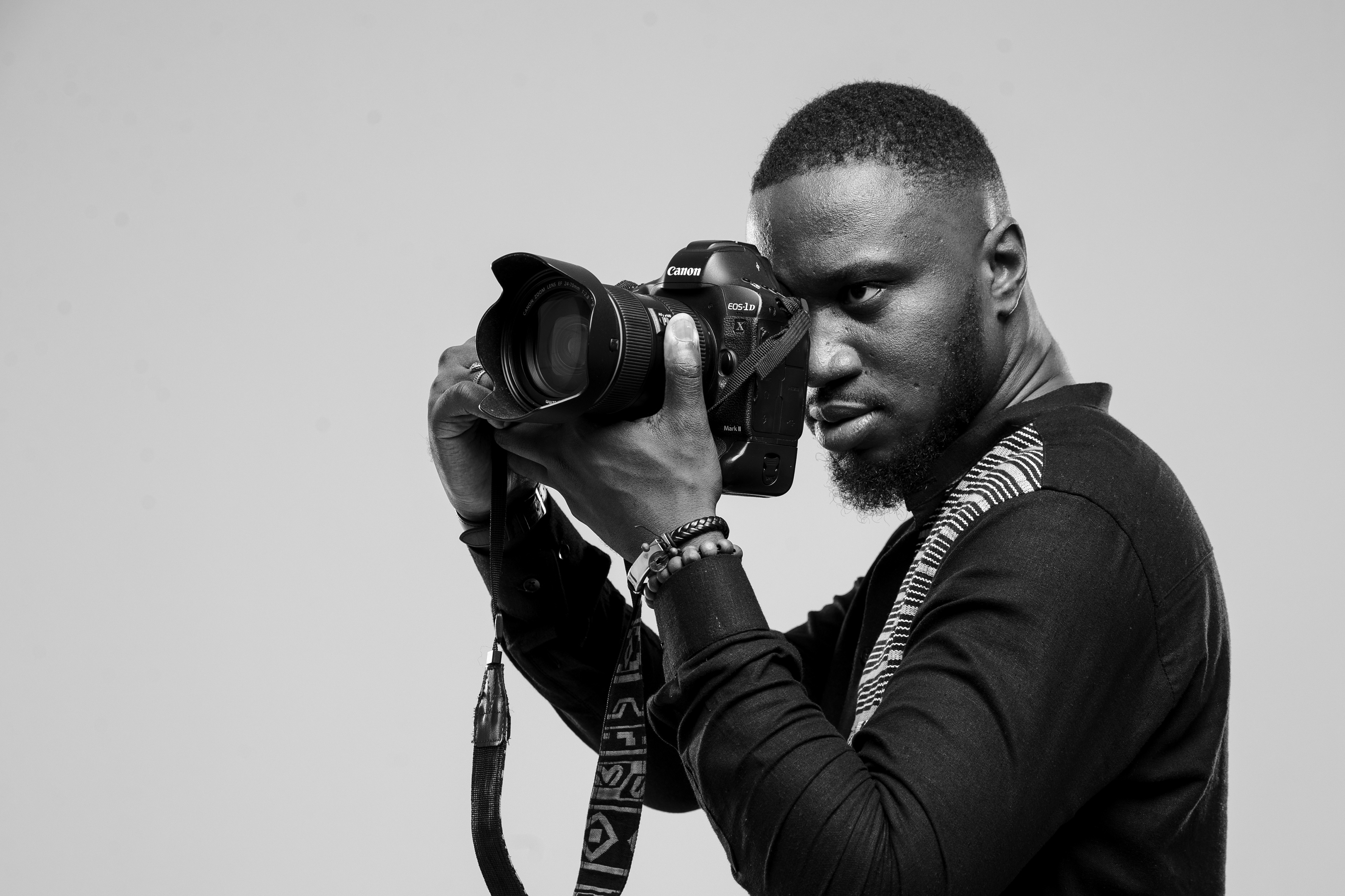 Black and white photo of Miléquêm Diarassouba, Photojournalist West Africa from Abidjan, Côte d'ivoire, holding a Canon EOS 1DX Mark II camera while working.