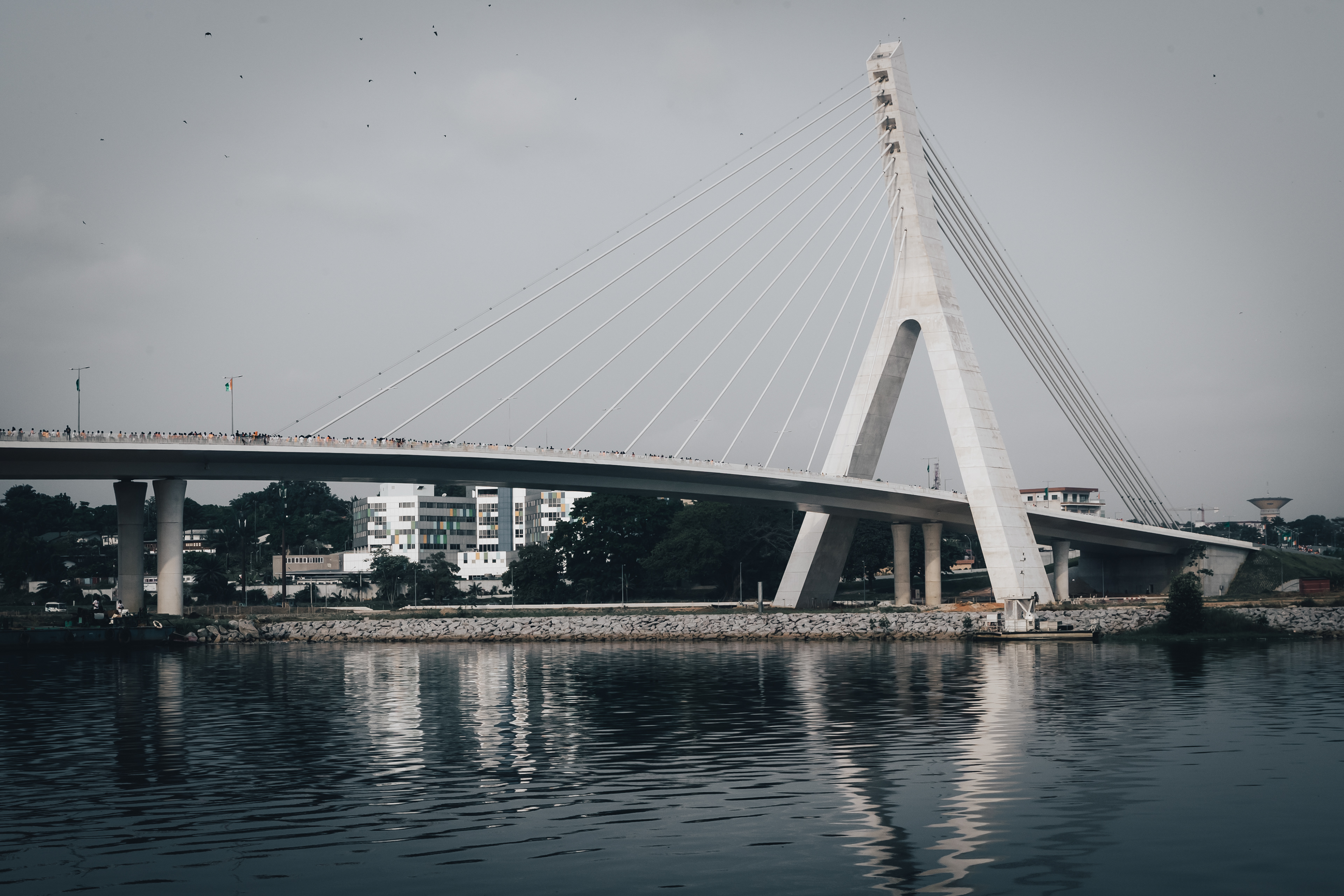 Photograph by Miléquêm Diarassouba, Photojournalist and Filmmaker: Detailed reflection of the Alassane Ouattara Bridge in the lagoon of Abidjan, showcasing its symmetrical architecture and elegance.