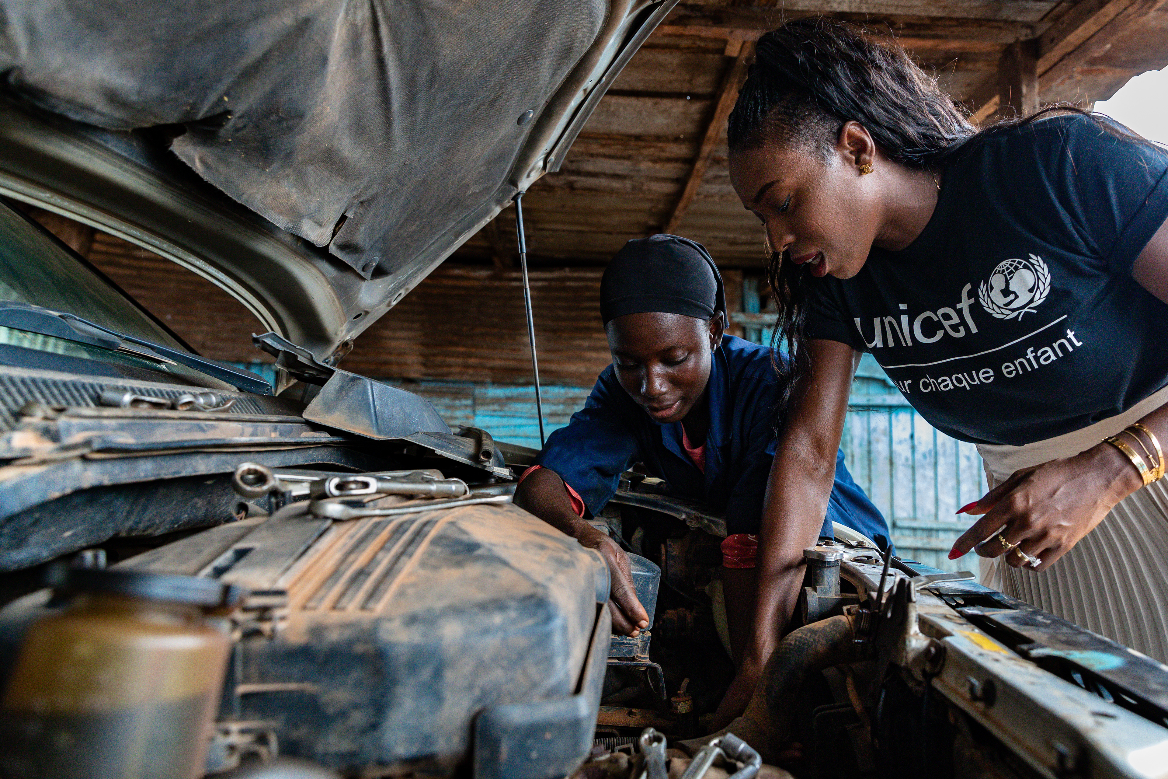Bernadette, 16, demonstrates engine disassembly to UNICEF Ambassador Murielle Ahouré Demps under a car hood in San Pedro, South-West Côte d’Ivoire, 14 October 2024, photographed by Miléquêm Diarassouba, Photojournalist West Africa.