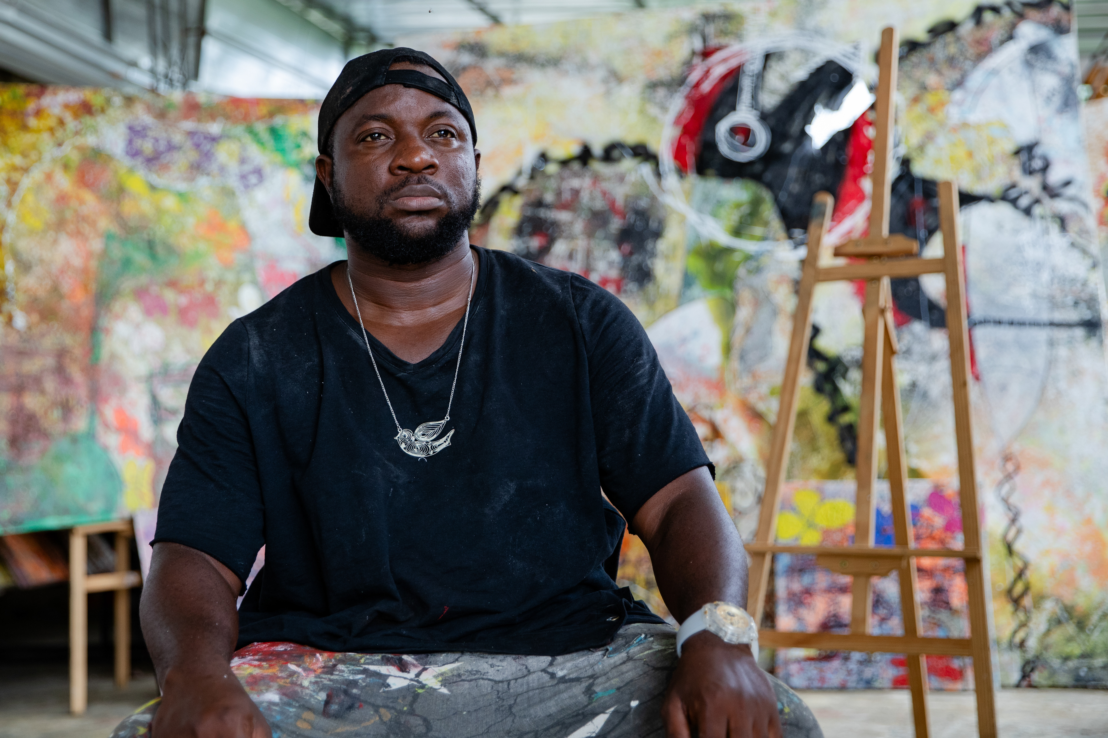 Ismael Tamek sitting in his Abidjan studio on November 3, 2023, with neo-expressionist artworks in the background, captured by Miléquêm Diarassouba, Photojournalist West Africa.