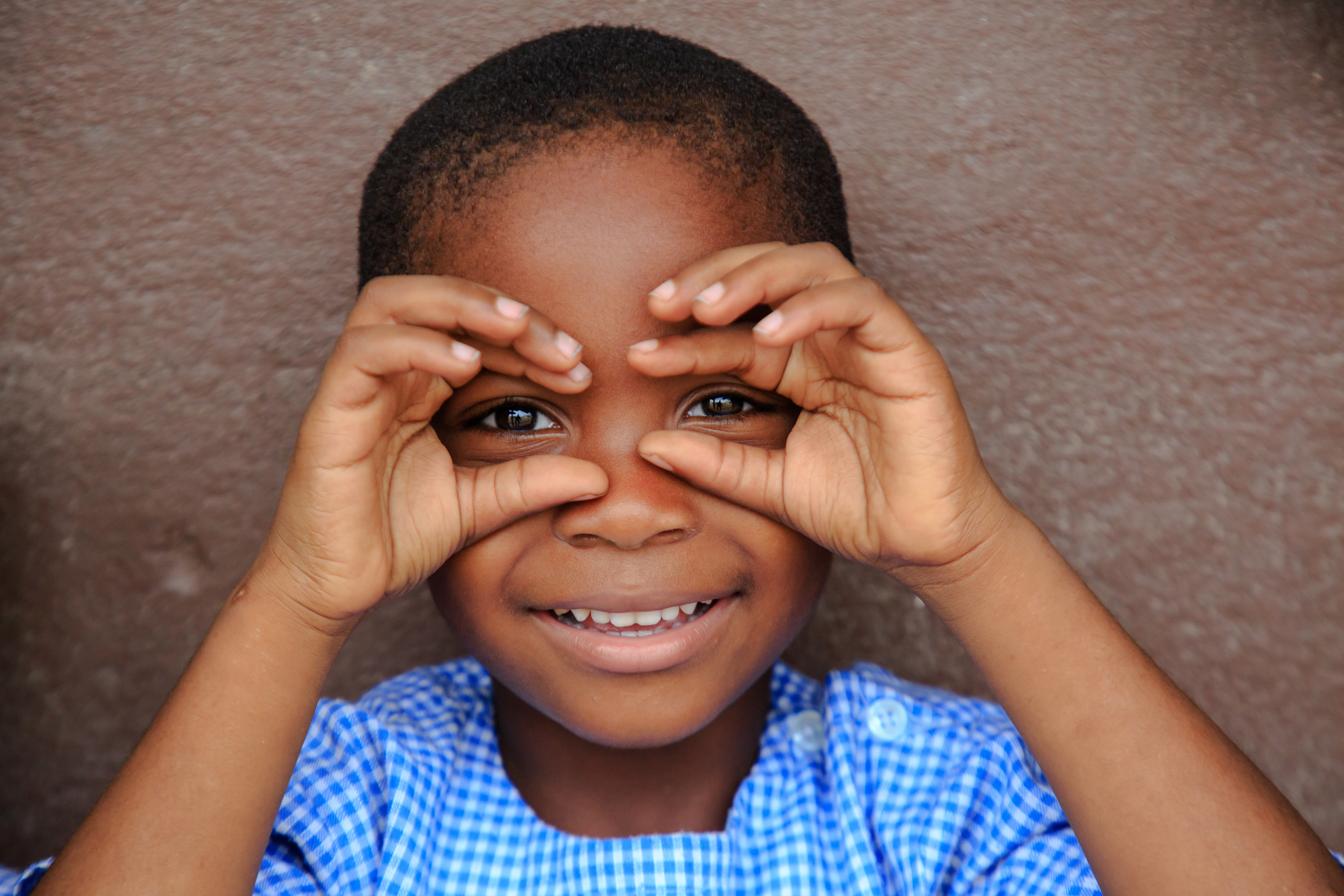 A child in a blue school uniform forms binoculars with their hands over their eyes at Gonzagueville Primary School in Abidjan, Côte d’Ivoire, on May 21, 2019. Captured by Miléquêm Diarassouba, Photojournalist West Africa, for UNICEF, highlighting children’s education.
