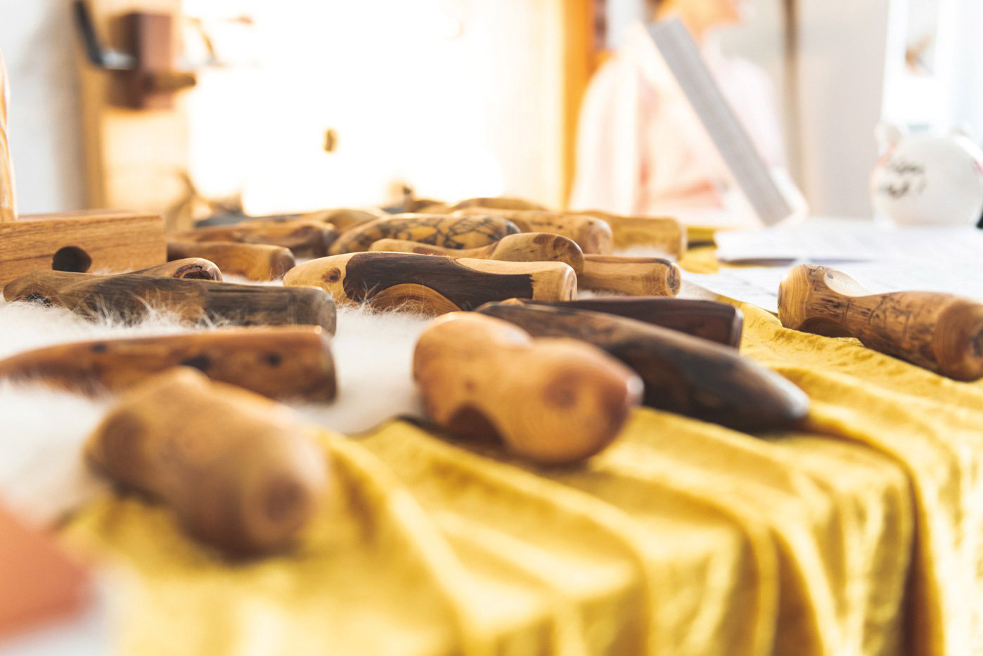 Aufreihung der Massage-Holzgeräte auf Tisch. Seitliche Aufnahme mit hoher Tiefenschärfe über den Tisch hinwegsehend.