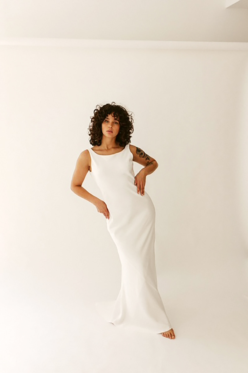 Modell mit weißem Brautkleid in minimalistischer Form vor weißer Hohlkehle stehend.