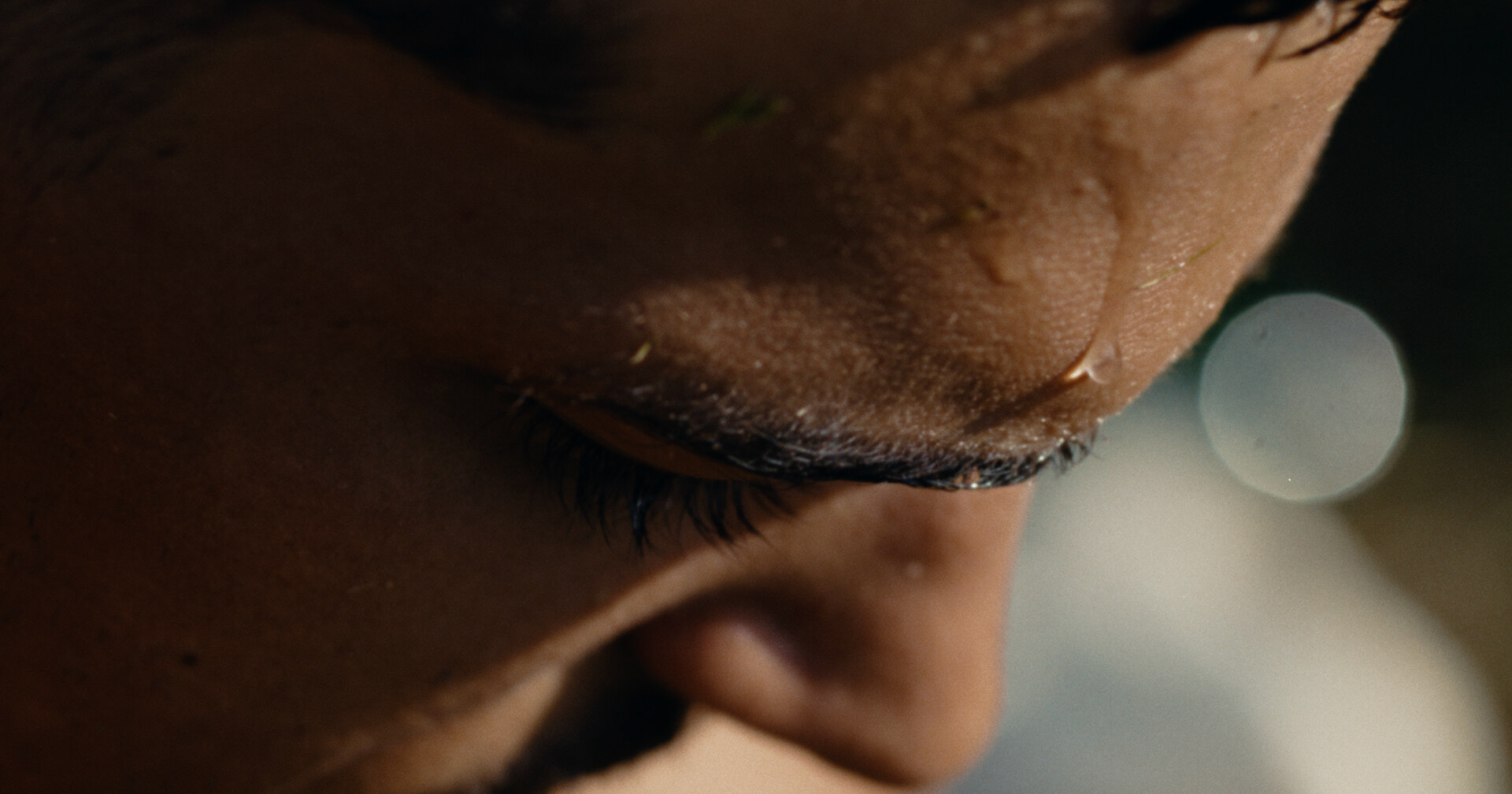 Ein Filmstill aus dem Film "TSHEGL". Eine Nahe an der in der sonne schwitzenden Stirn des Protagonisten.