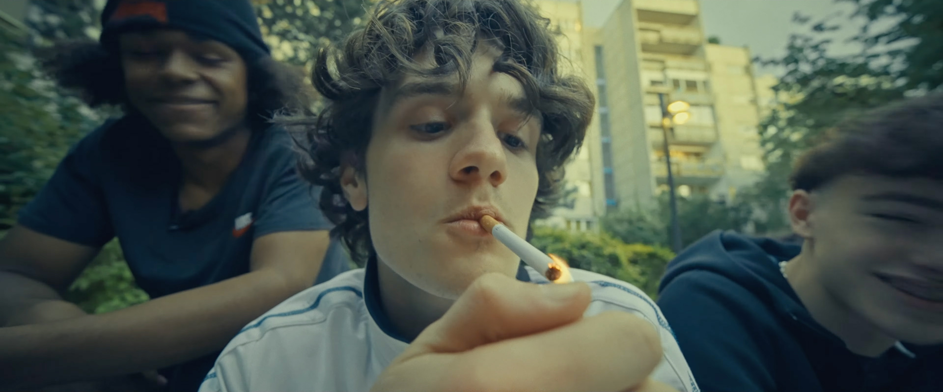 Ein Filmstill aus dem Film "zwischen". Der Protagonist Zündet sich eine Zigarette an neben ihm sitzen zwei weitere Jungs.