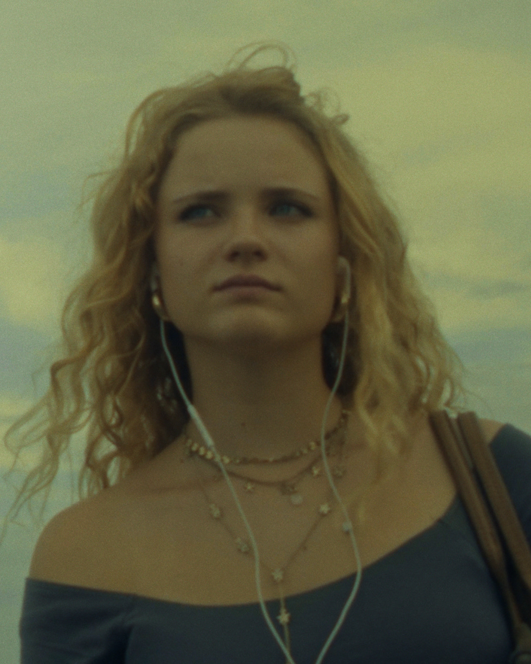 Ein Filmstill aus dem Film "zwischen". Die Haupdarstellerin vor bewölktem Himmel mit Kabelkopfhörern in ihren Ohren.