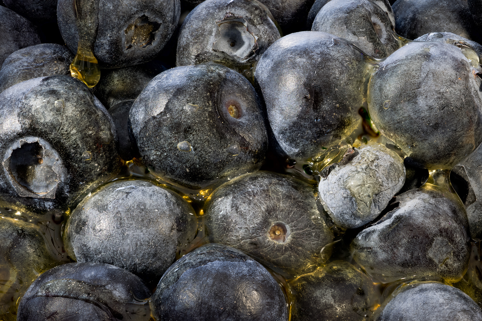Macro photography of organic blueberries coated in golden honey, creating a cosmic texture that resembles alien spheres or planets.