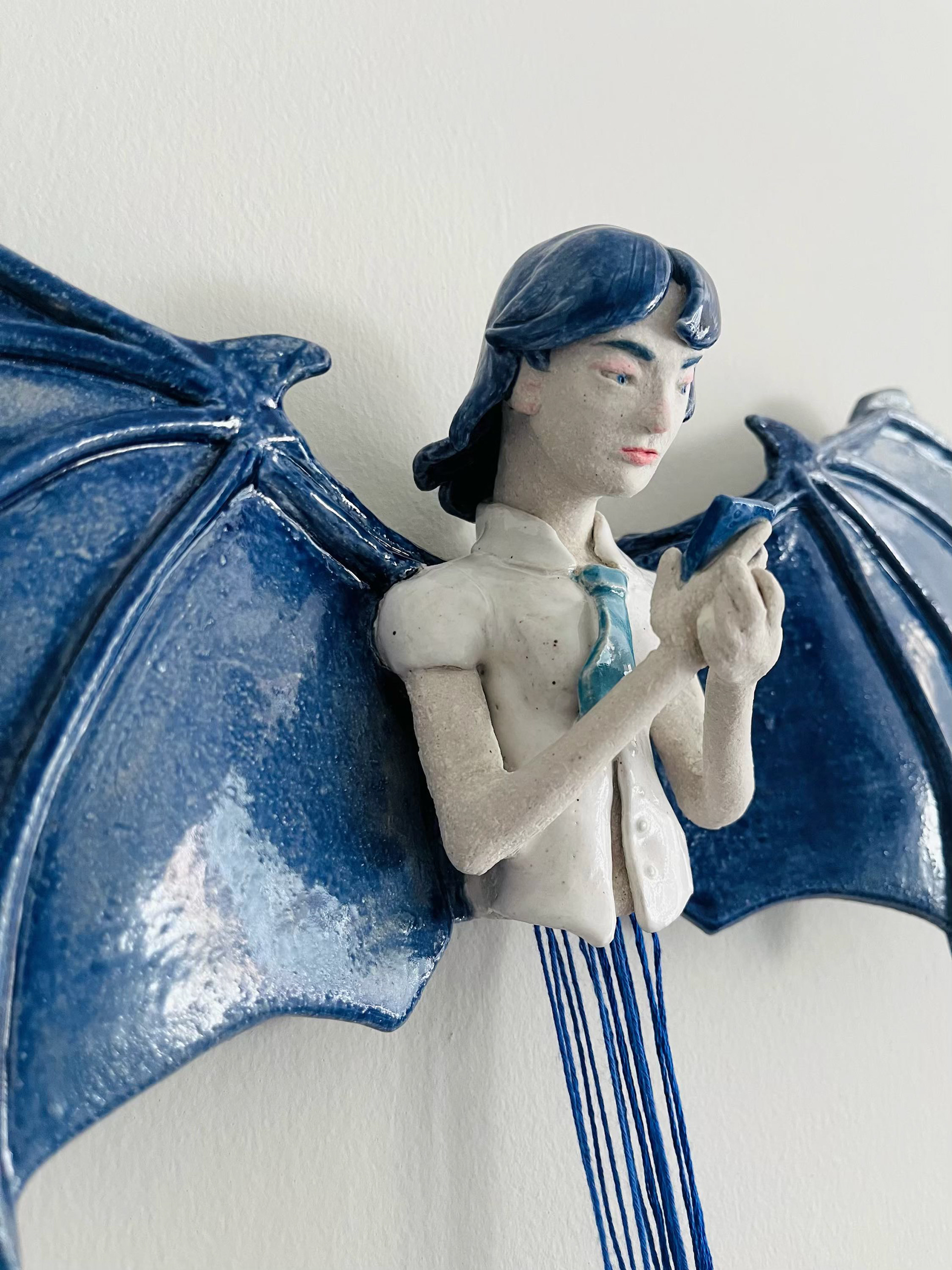 The top portion of the sculpture hangs on the wall, separate from the body and connected by very long threads.