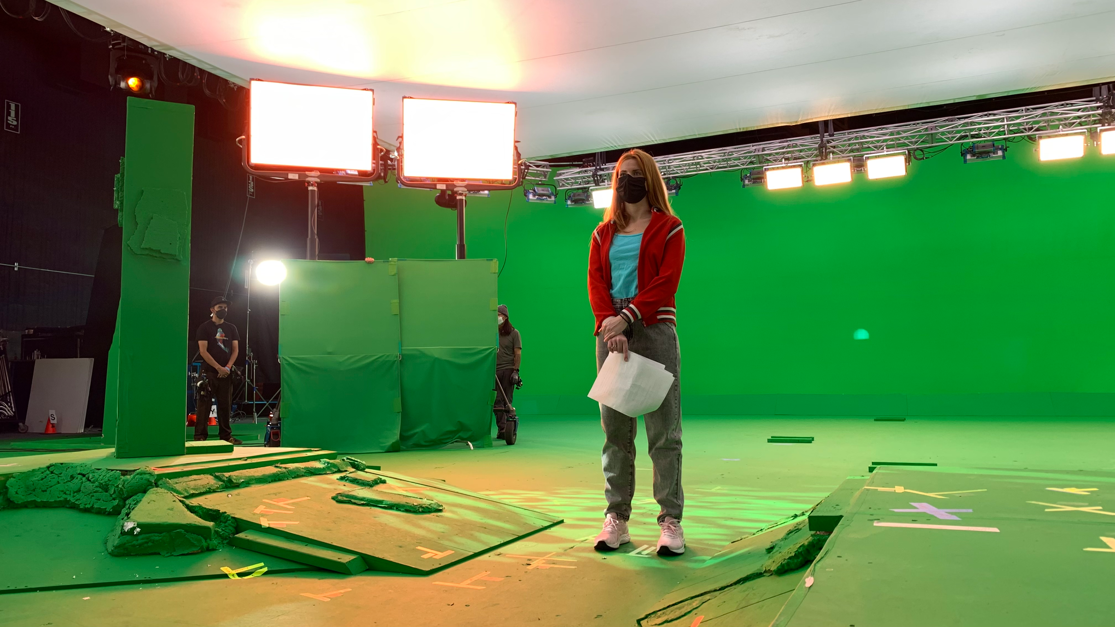 Actor in a red jacket standing in front of a green screen on a soundstage during filming