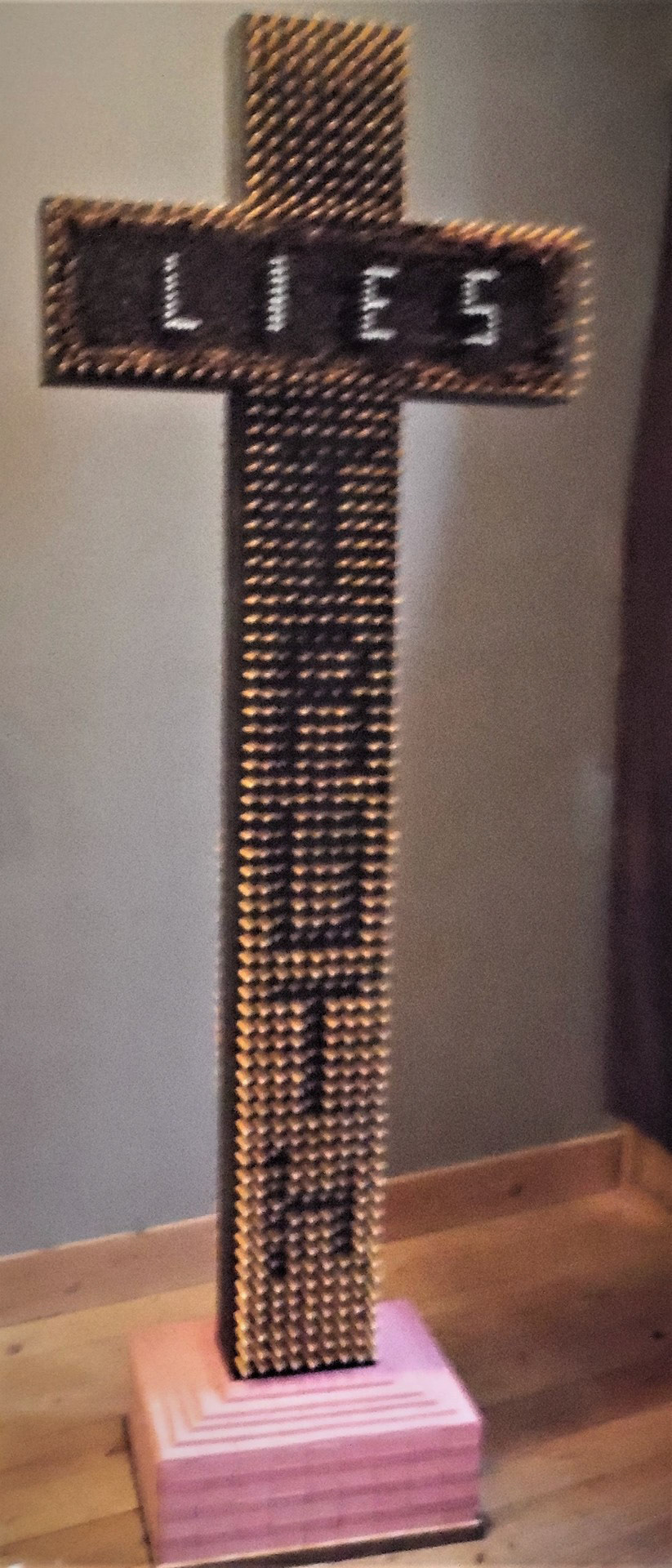 Christian cross penetrated with pencils that contain the words Lies and Truth secured in a base made of pin pearl erasers.