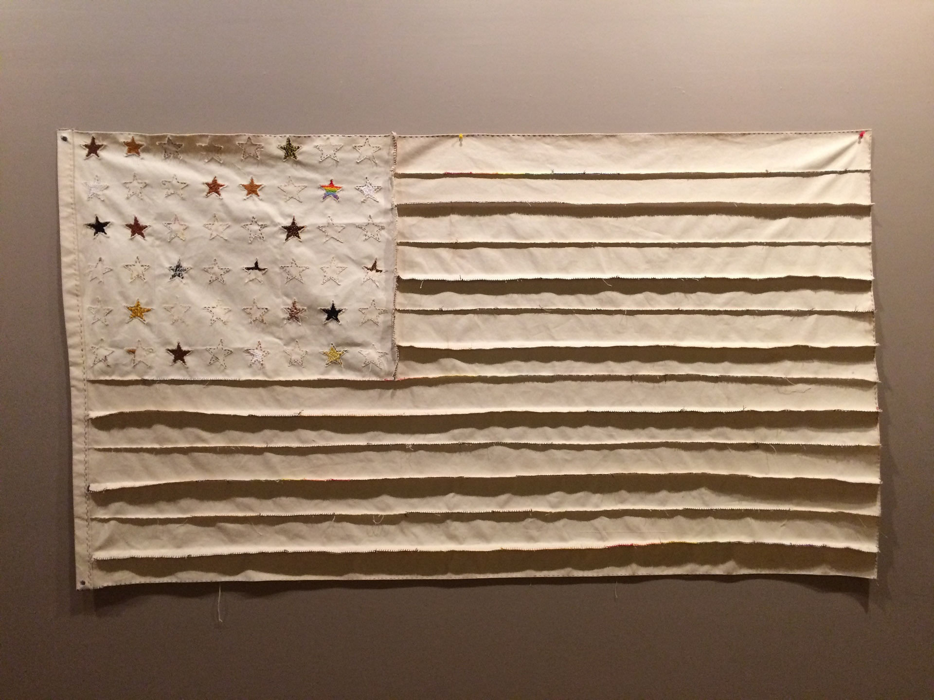 Flag sewn from strips of canvas with the emphasis on the different color threads used to bind the flag as a metaphor representing what holds America together are the different ethnic citizens.