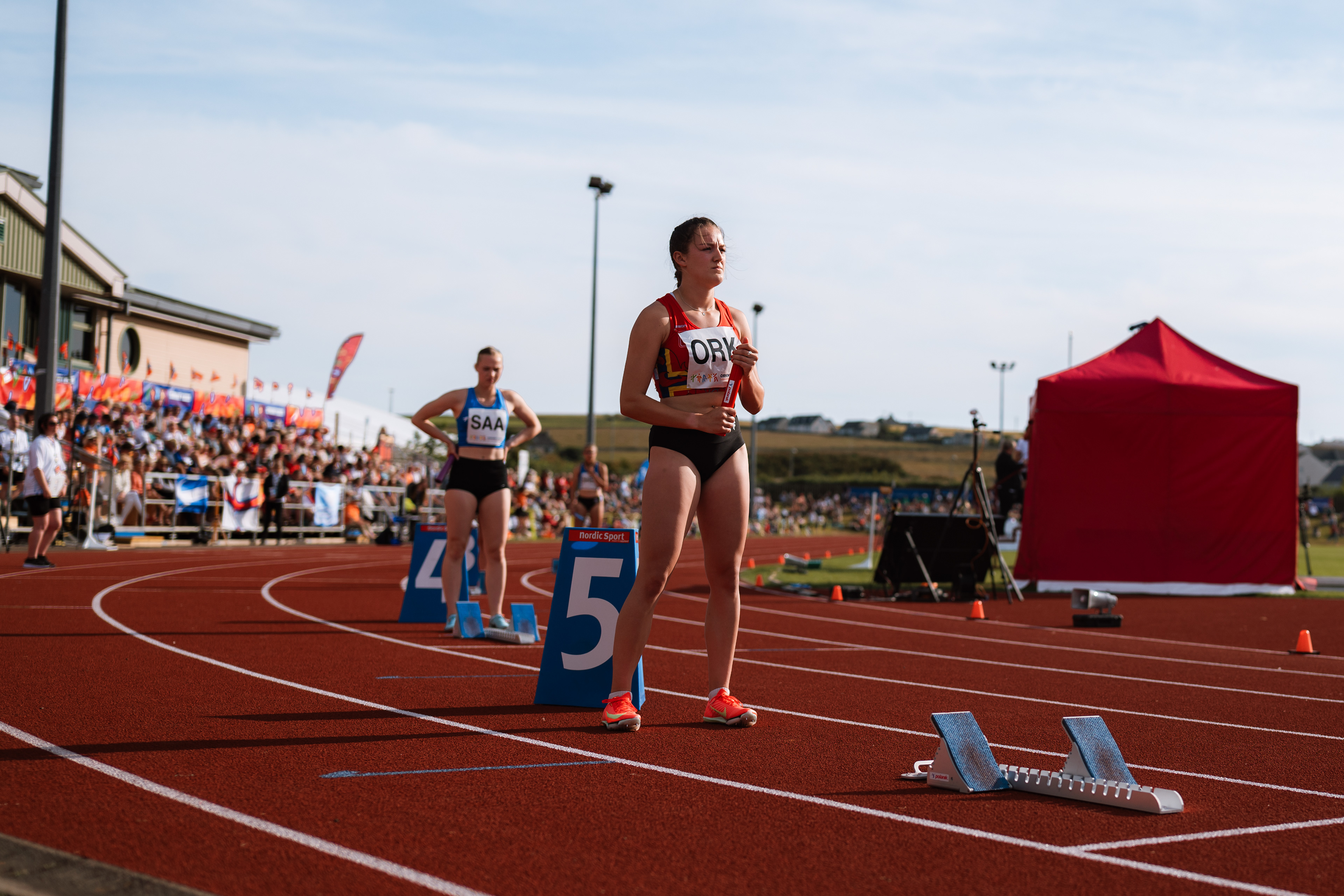 Athletes competing at Orkney 2025 Island Games Athletics venue with professional branded look & feel.