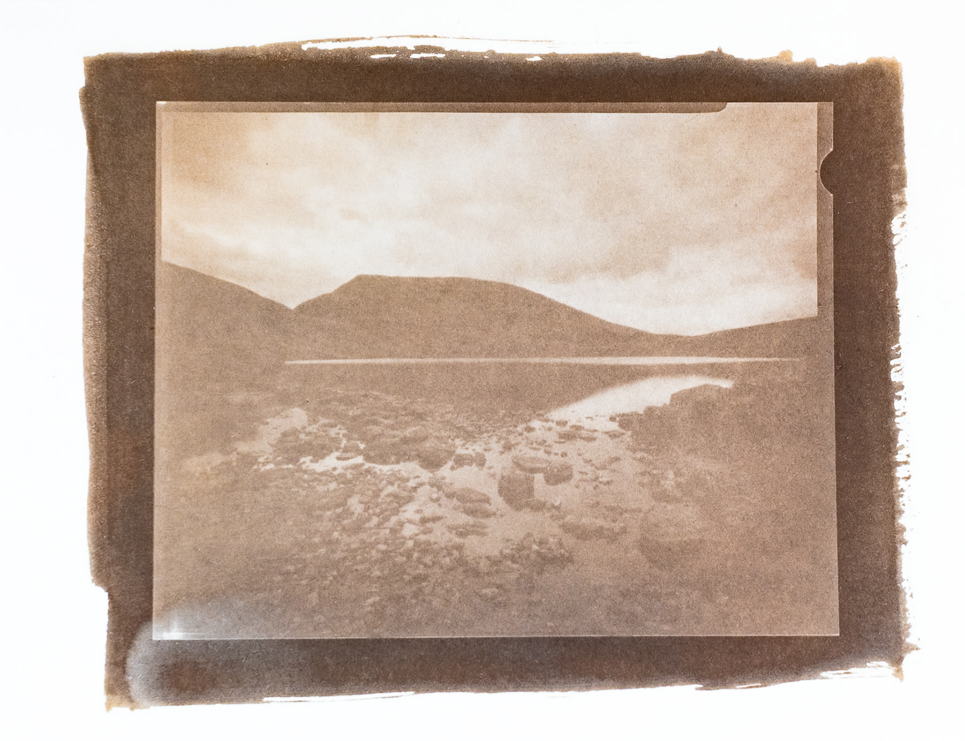 Fine art hand printed argyrotype print of the rocky shore of a Lakeland tarn, with a rolling mountain horizon.