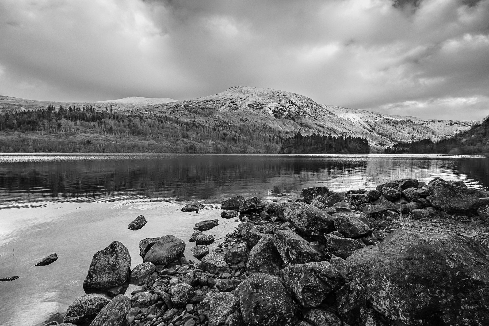 A black and white image of  a calm Thirlmere Reservoir and the snow capped lower slopes of the Helvellyn Range.