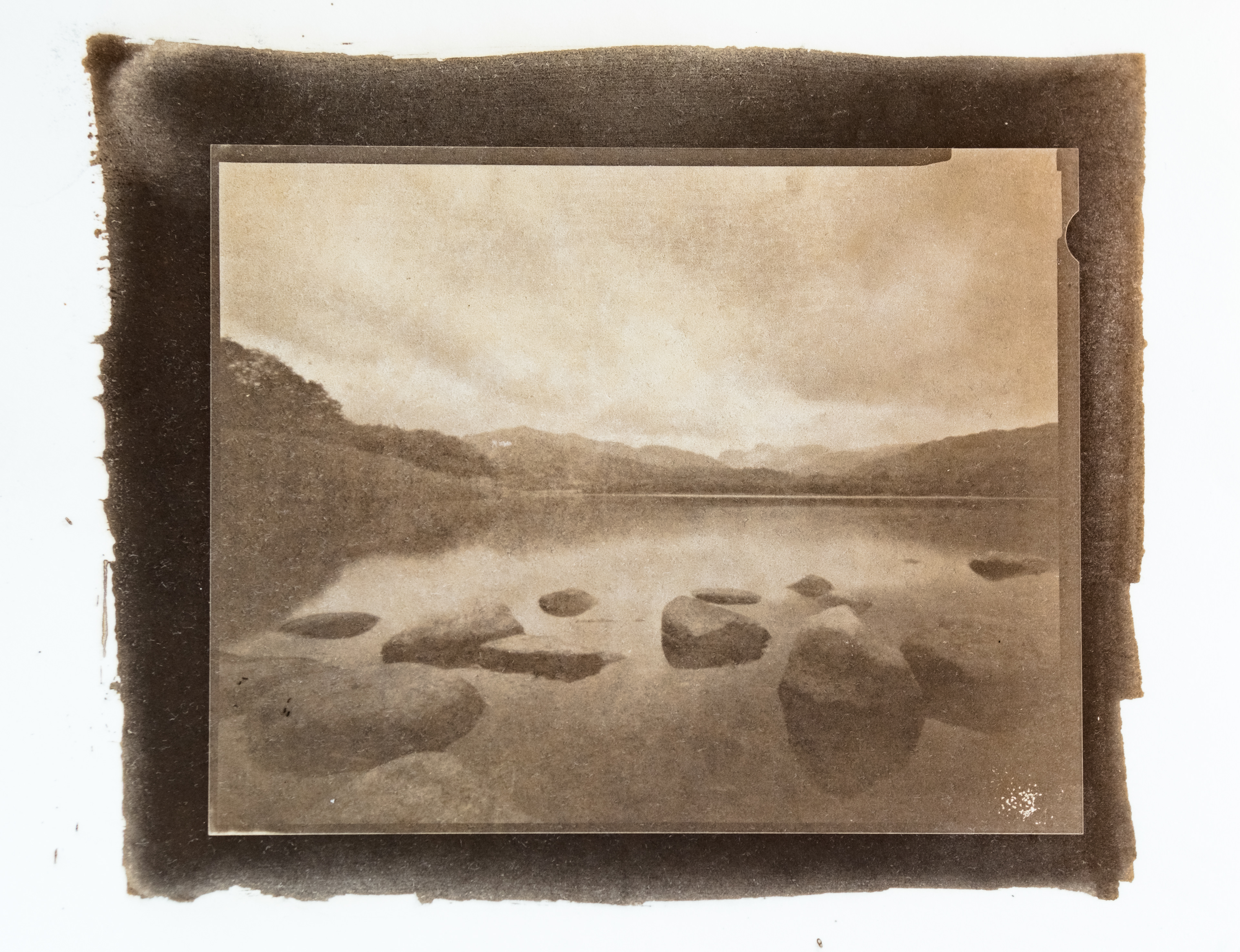 A fine art print using the Argyrotype process. The image shows the rocky shore of Elterwater in the Lake District with the Langdale Pikes in the distance.