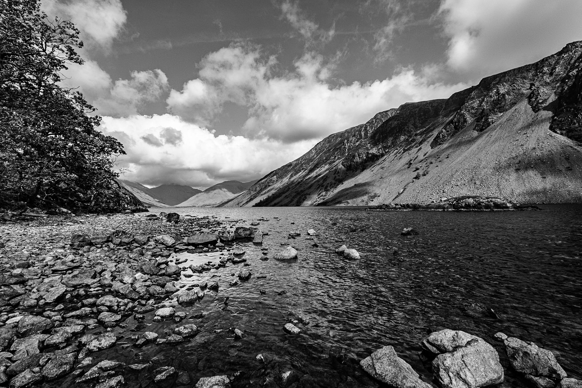 A black and white view of Wastwater and the Wasdale Screes set against a striking sky with billowing white clouds