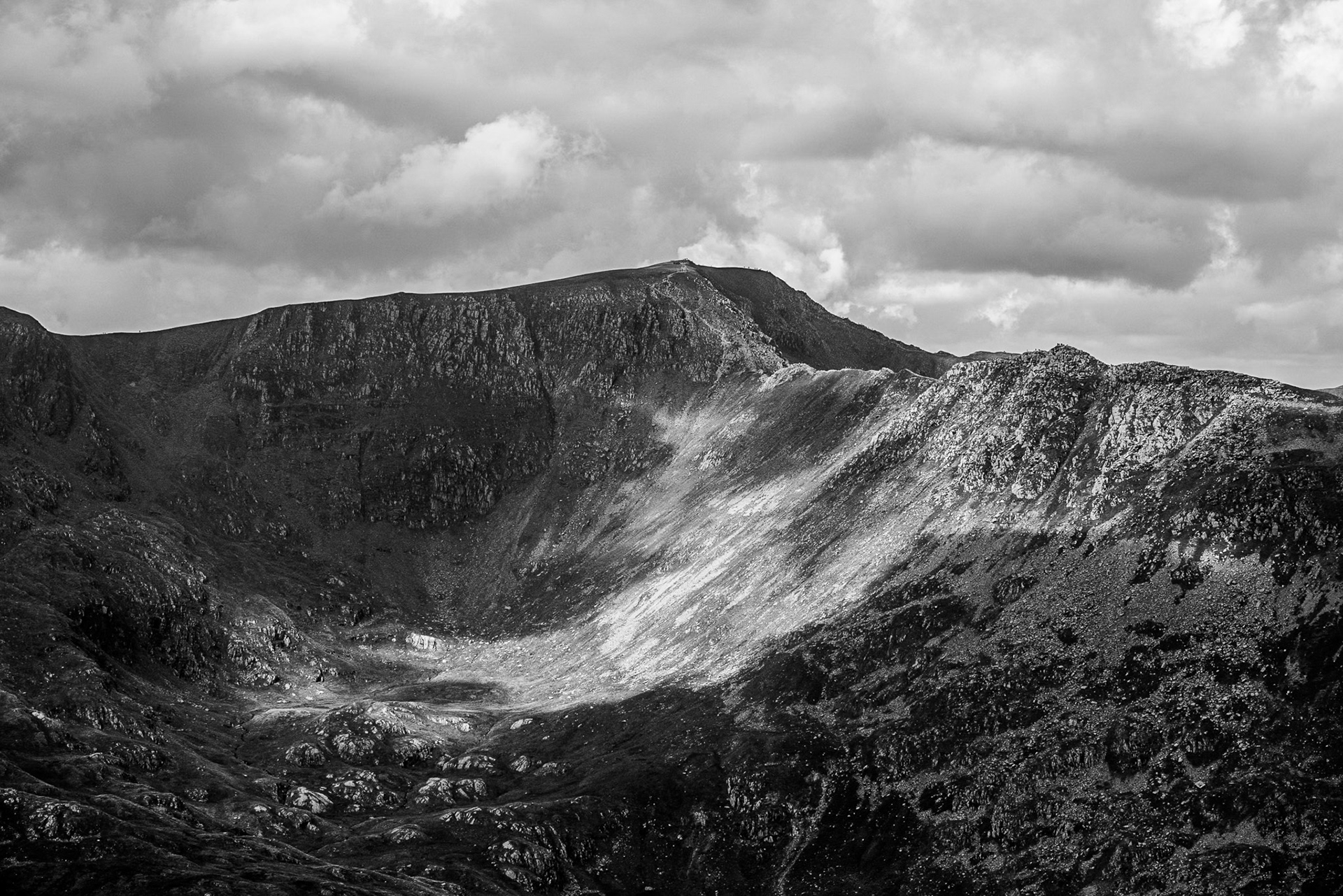 Black and white shot of patches of sunlight highlighting the steep slopes of Striding Edge in the Lake District. 