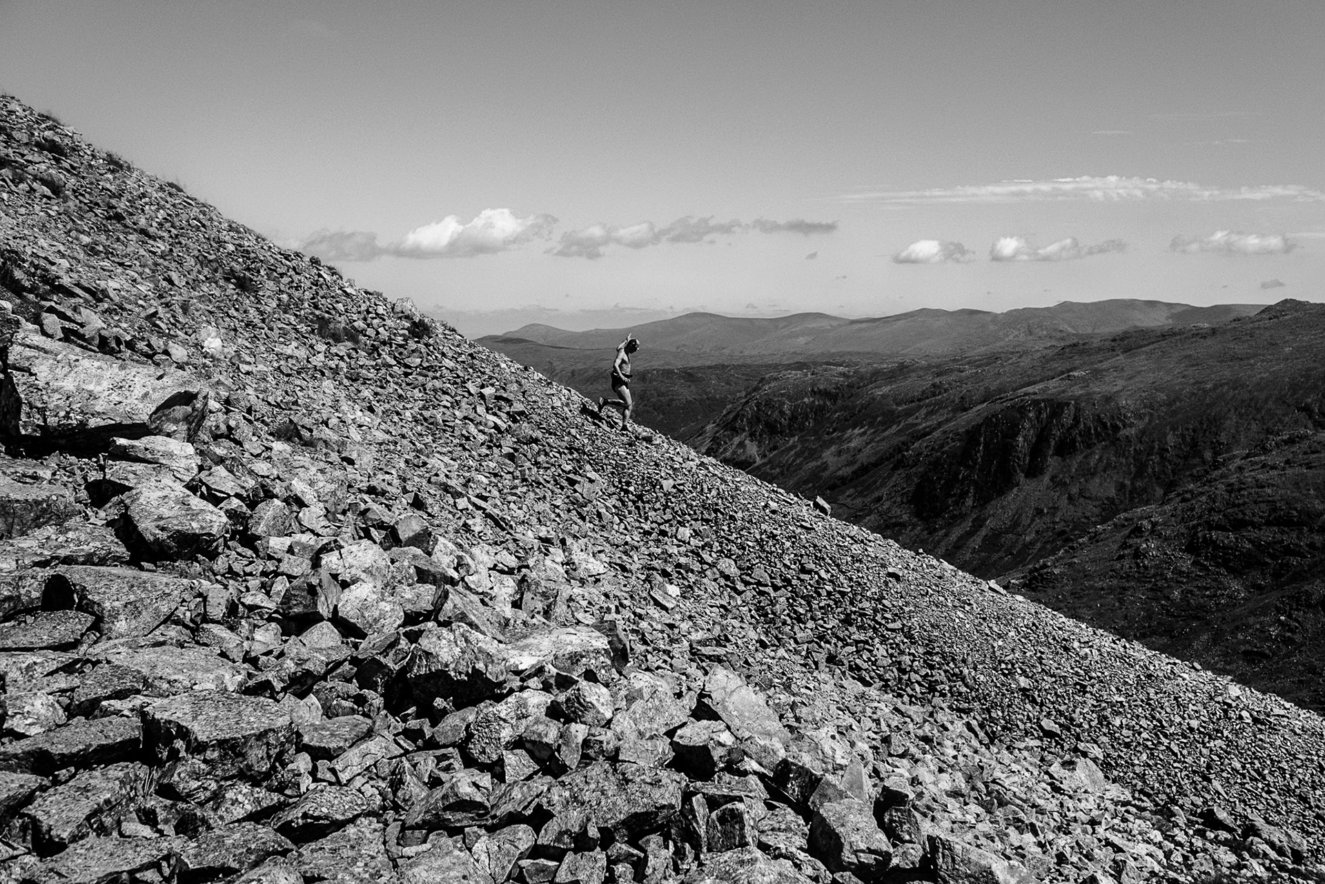 Dramatic black and white shot of a Fell Runner descending a very steep scree slope under a clear blue summer sky.