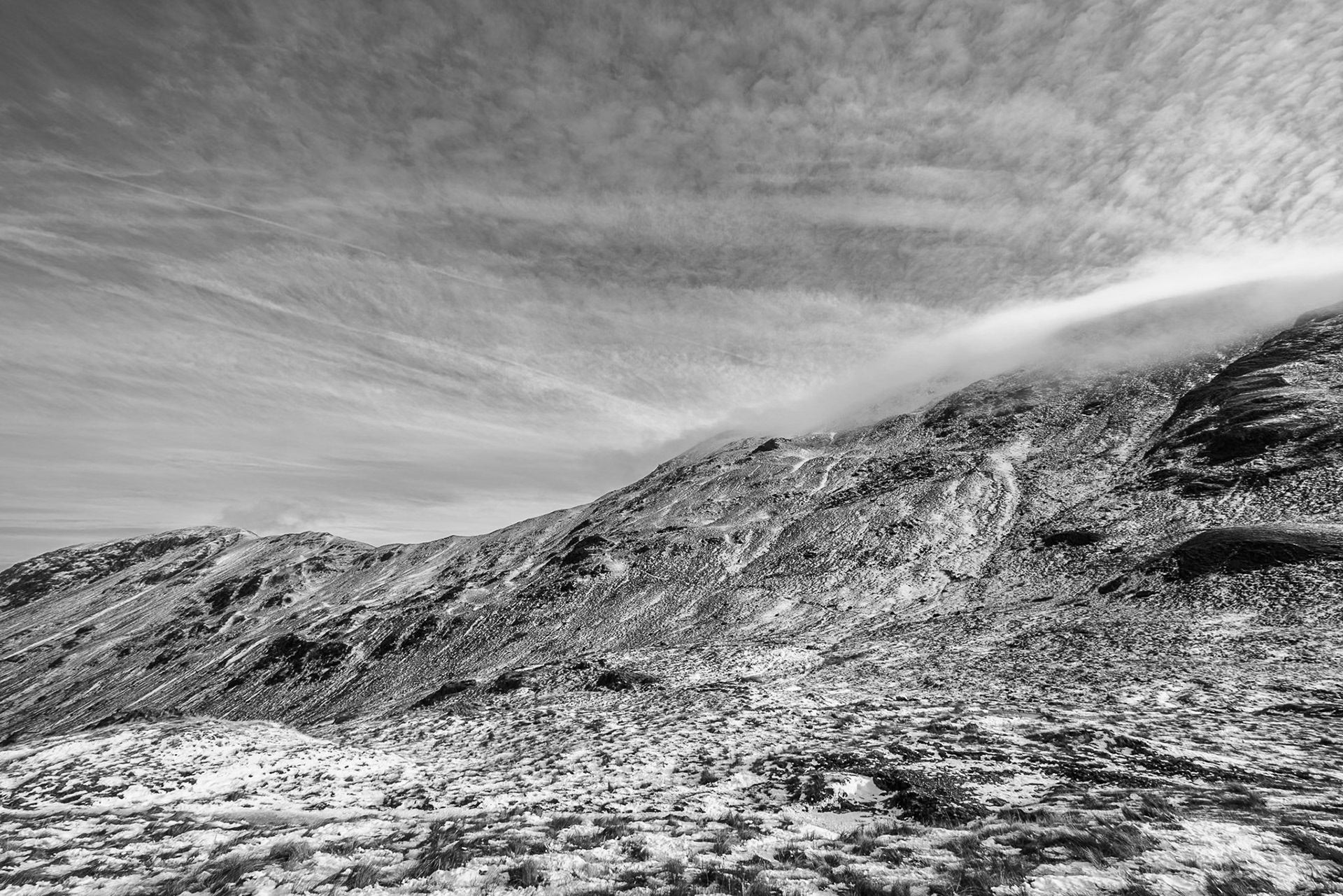 A shot of the icy slopes of St Sundays Crag under a bright winter sky with high scattered cloud.  The shot is rendered in black and white.