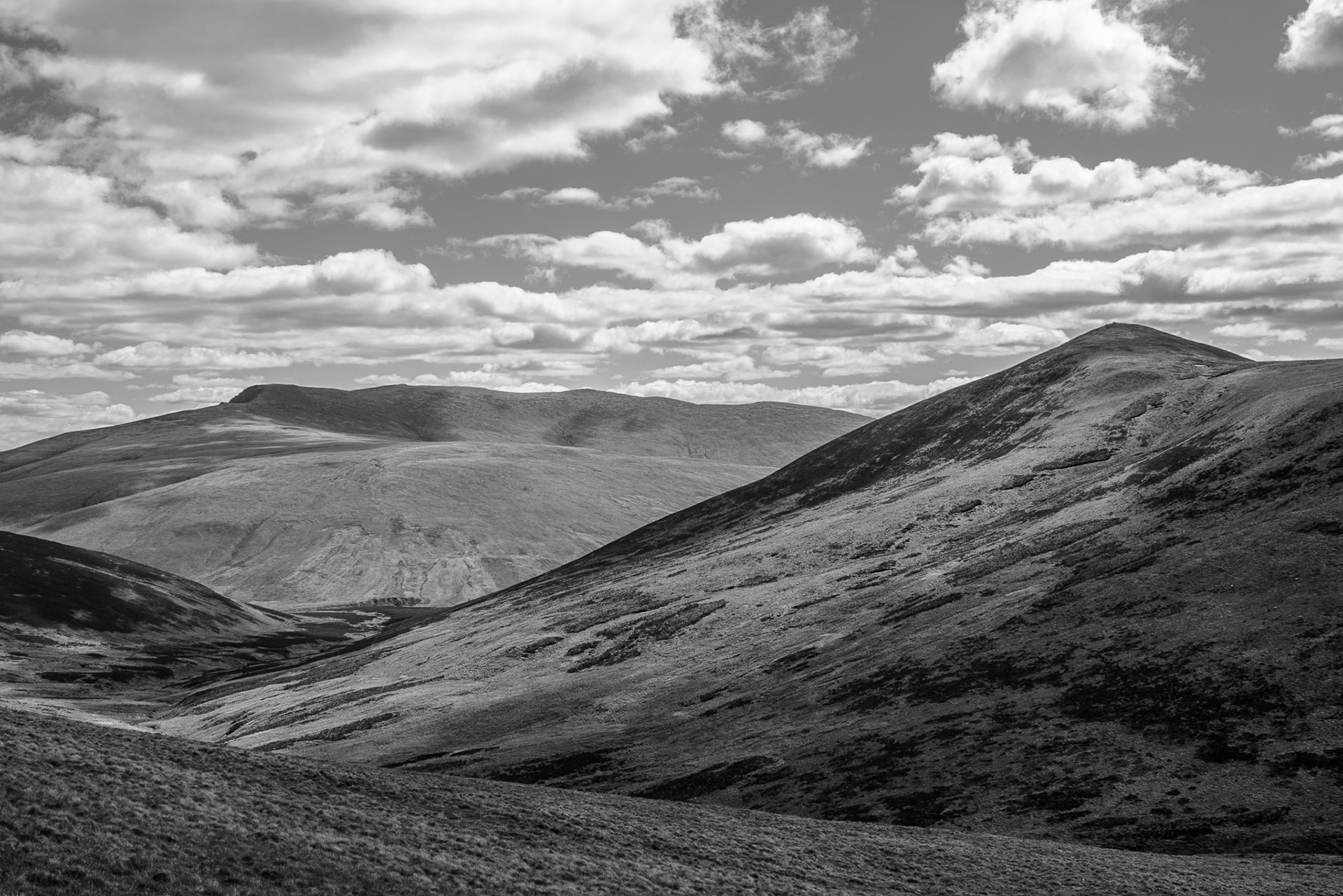 Black-and-white image showing Blencathra and Carrock Fell in the English Lake district  beneath scattered clouds, creating a quiet, expansive, dramatic mood.