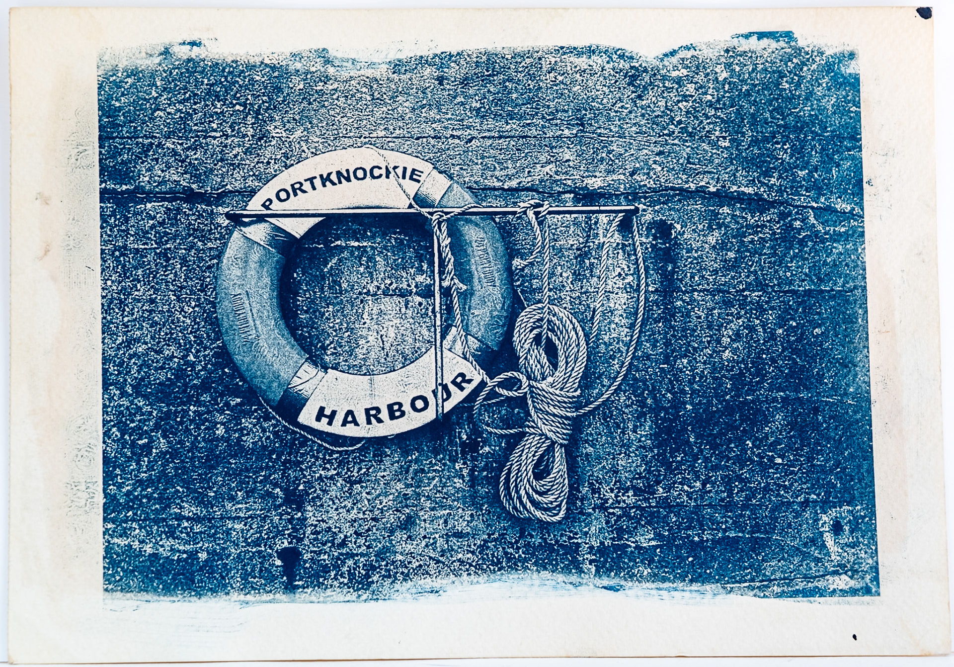 Fine art cyanotype print from a digital negative showing a Lifebuoy and rope on a harbour wall.  The words Portknockie Harbour are print on the life buoy.