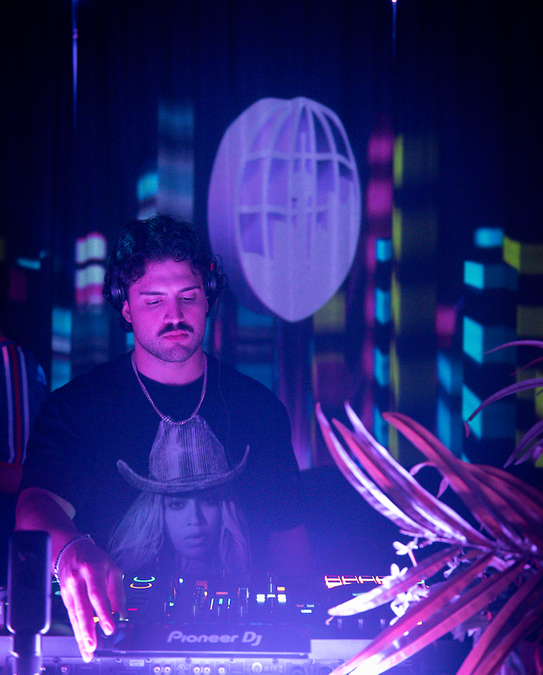 Caption: DJ Derose mixes electronic tracks under neon lighting while performing a live set at Bar Dem in Toronto on Thursday, Jan. 29, 2026. The DJ helped cultivate a vibrant, energetic atmosphere for the crowd's fun night out in the city. Camera Settings: 1/60, ISO 6400, f/2.8