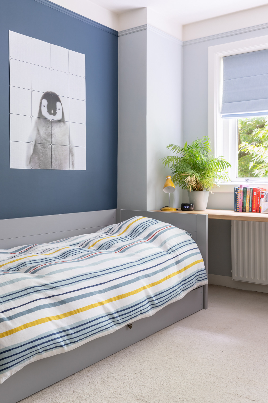 Interieur blauwe slaapkamer met grijs bed en pinguïn muurdecoratie