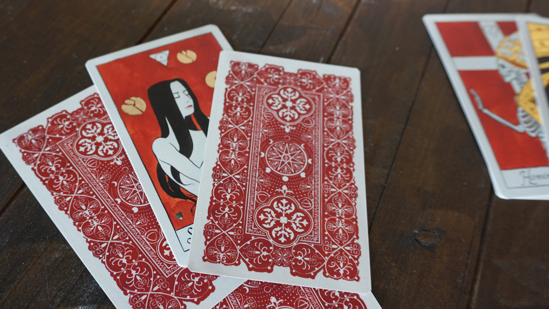 Strigarum Arcana tarot cards displayed on a wooden table, showing the red card backs and illustrated Major Arcana.