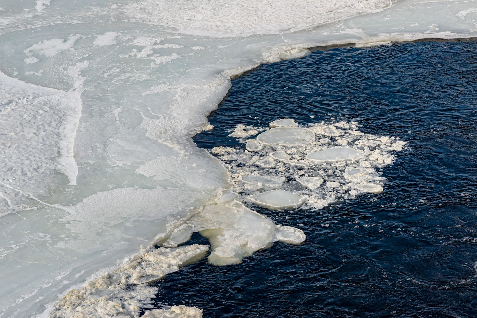 The solid ice and water divide the frame along a diagonal, and a circular area of broken ice framed within the water is the center of interest.