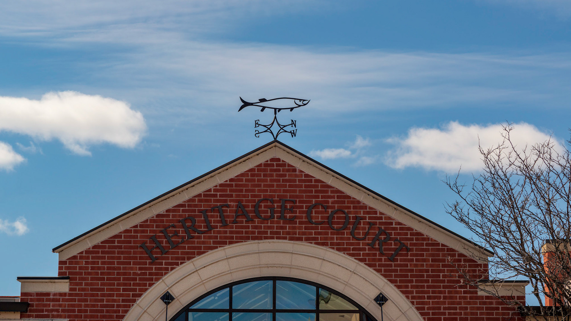 An interesting weather vane with a building pointing towards it and clouds symmetrically placed on either side.