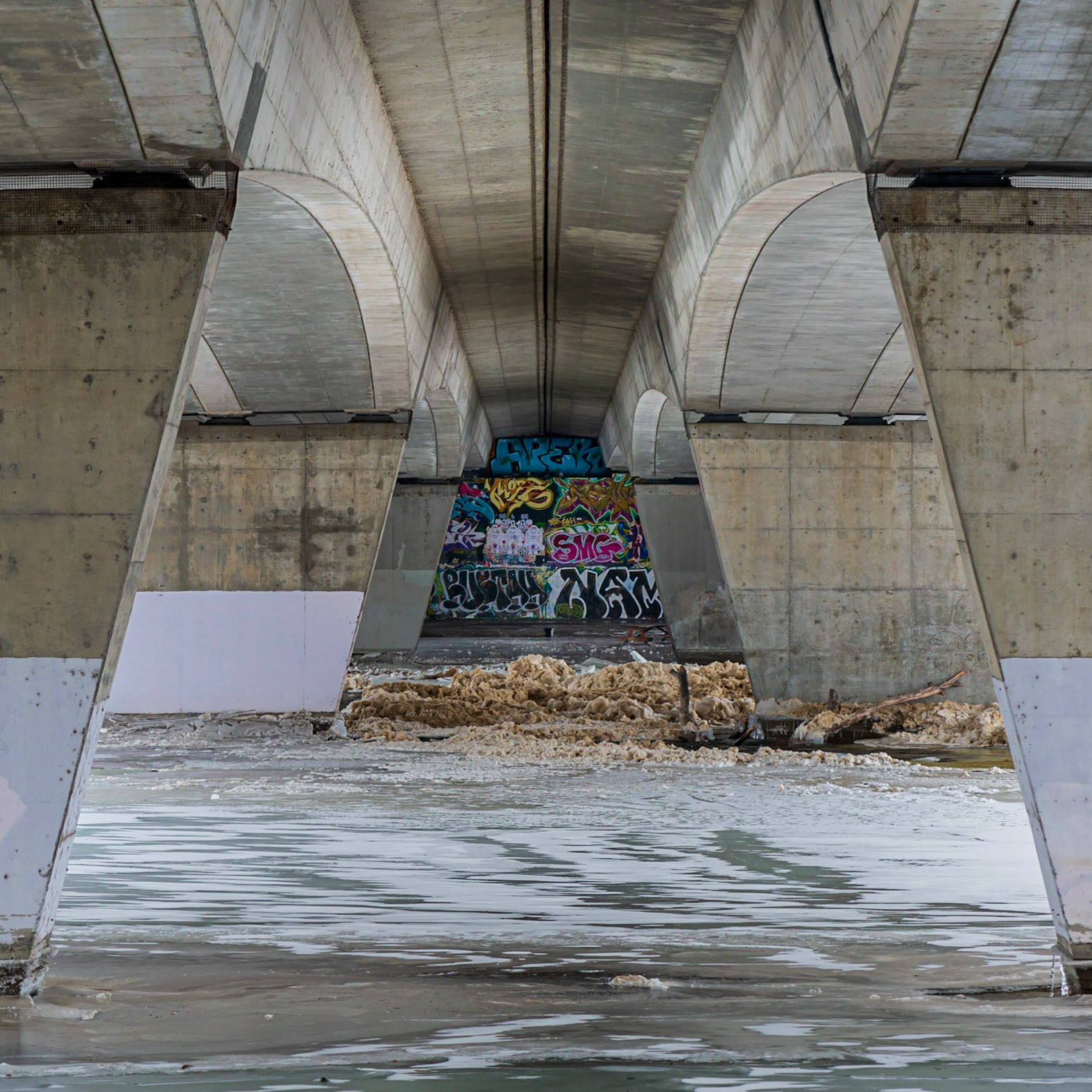 The view of the Rideau River under the Bronson Street bridge. I chose the camera position and cropping to emphasize the symmetry and frame the graffiti in the distance. The compression of distance by the 105 mm lens gives the eye a puzzle to figure out as well.