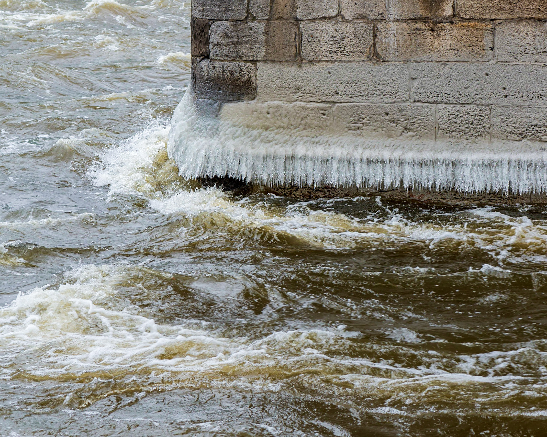 A pillar under the Heron Road bridge, with a skirt of icicles near the water line. I wanted to draw attention to the icicles and took several shots. I selected this shot because the two lines of turbulent water echo and reinforce the line of icicles.
