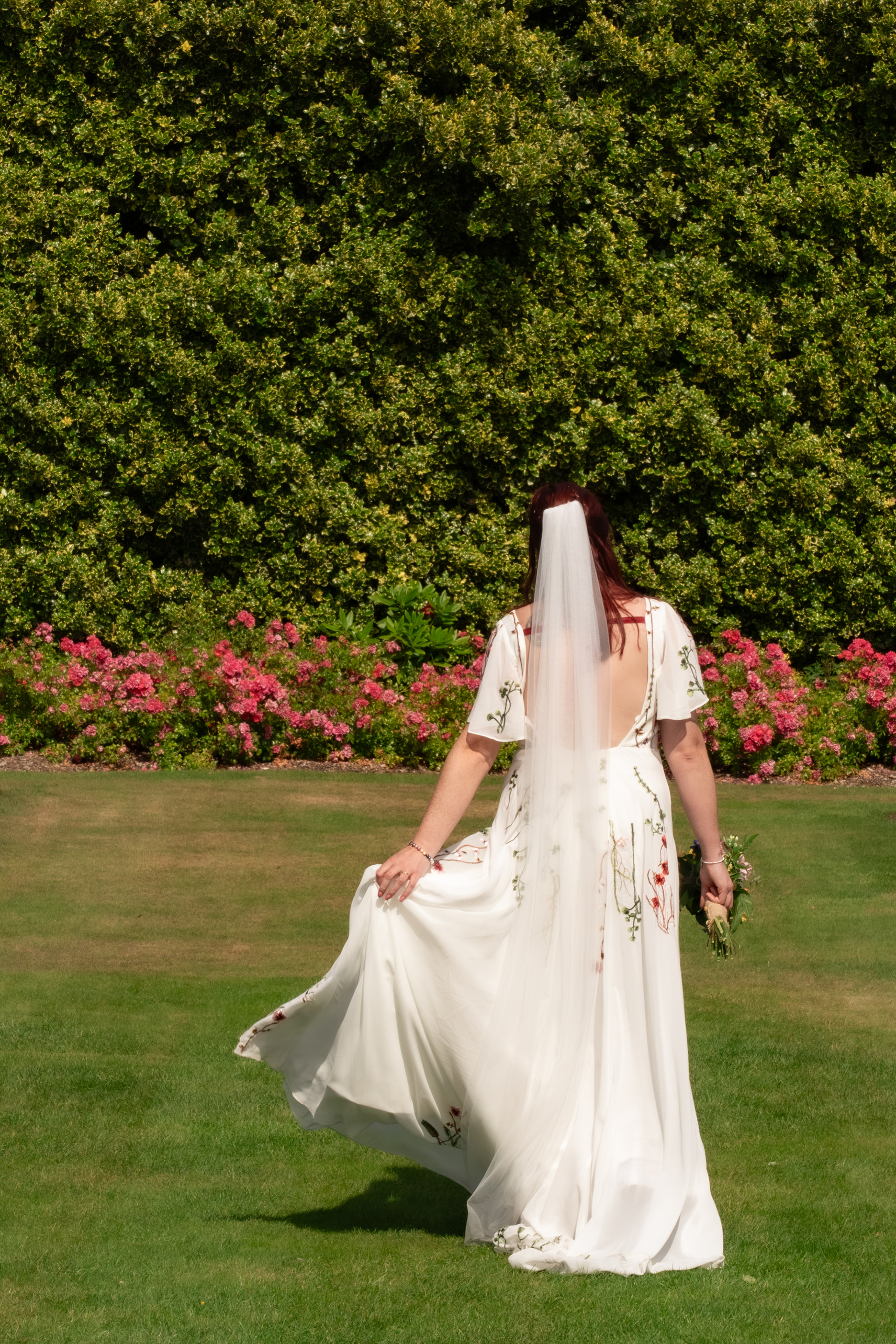 A bride in a white dress with floral embroidery swishes her skirt as she walks away from the camera.