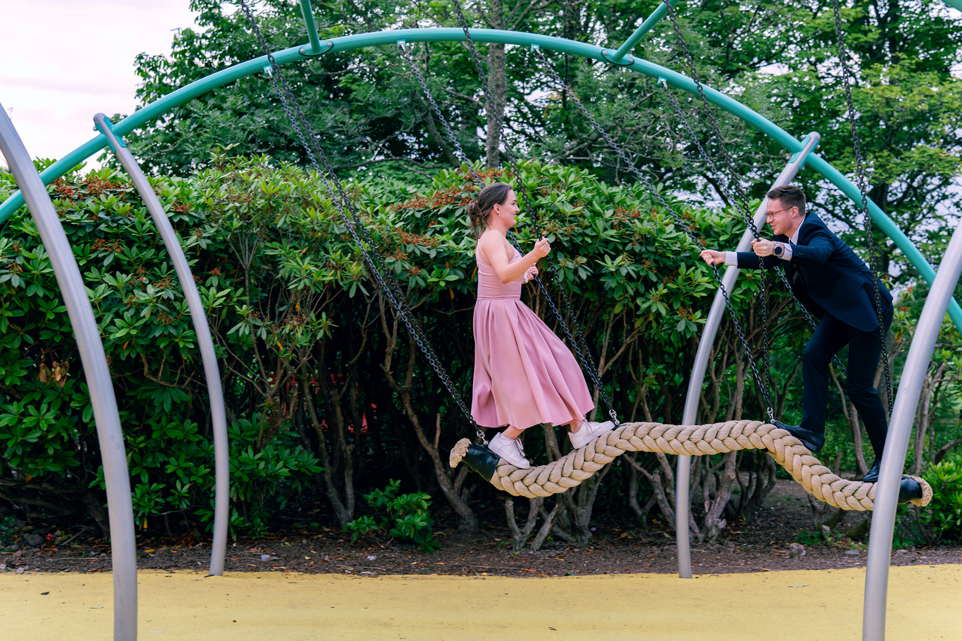 A woman in pink and man in navy play on the swings during an Aberdeen wedding