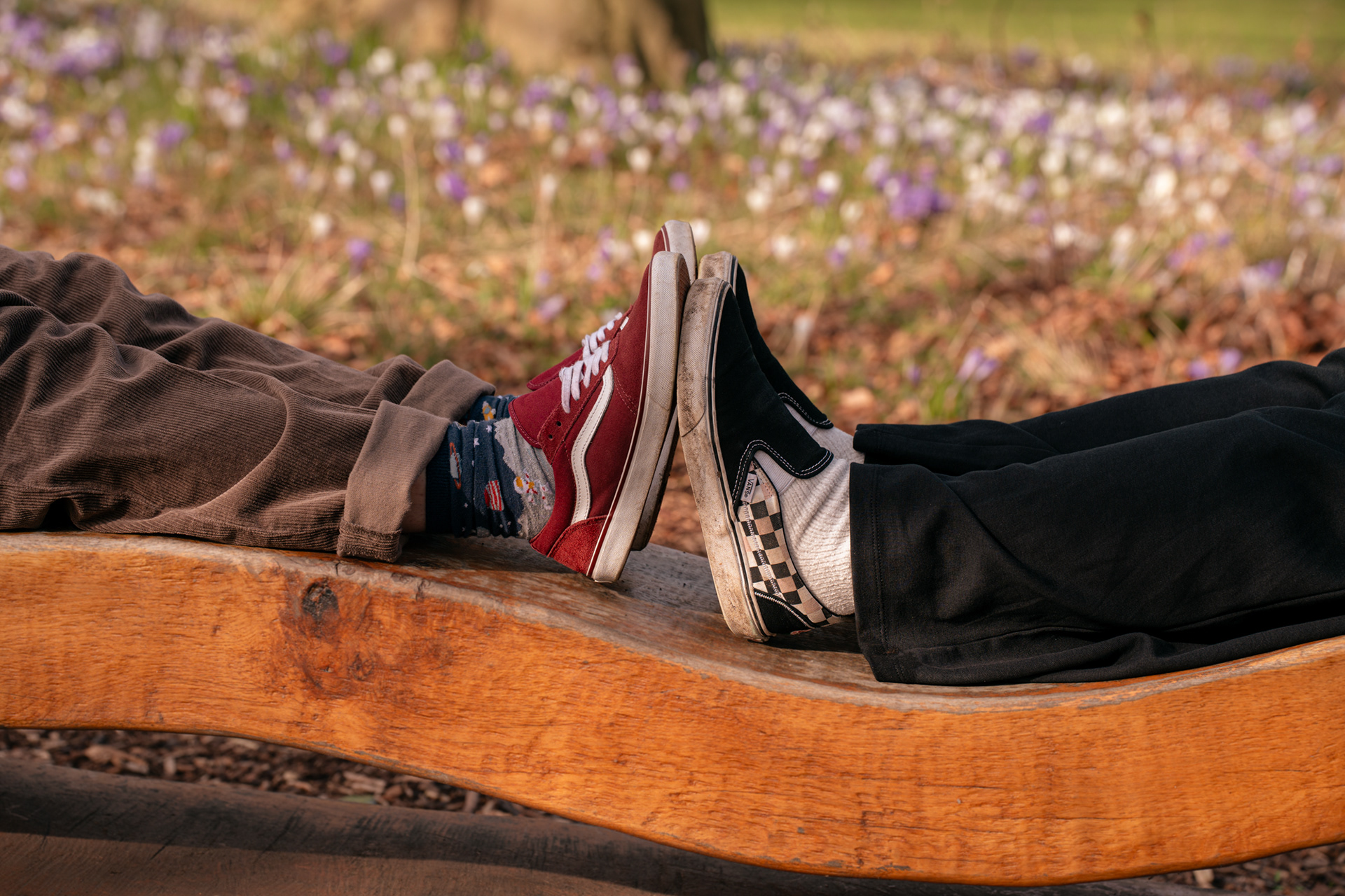 Close up of two pairs of feet in trainers pressed sole to sole, on an ornamental bench in Aberdeen. Crocuses show behind them.