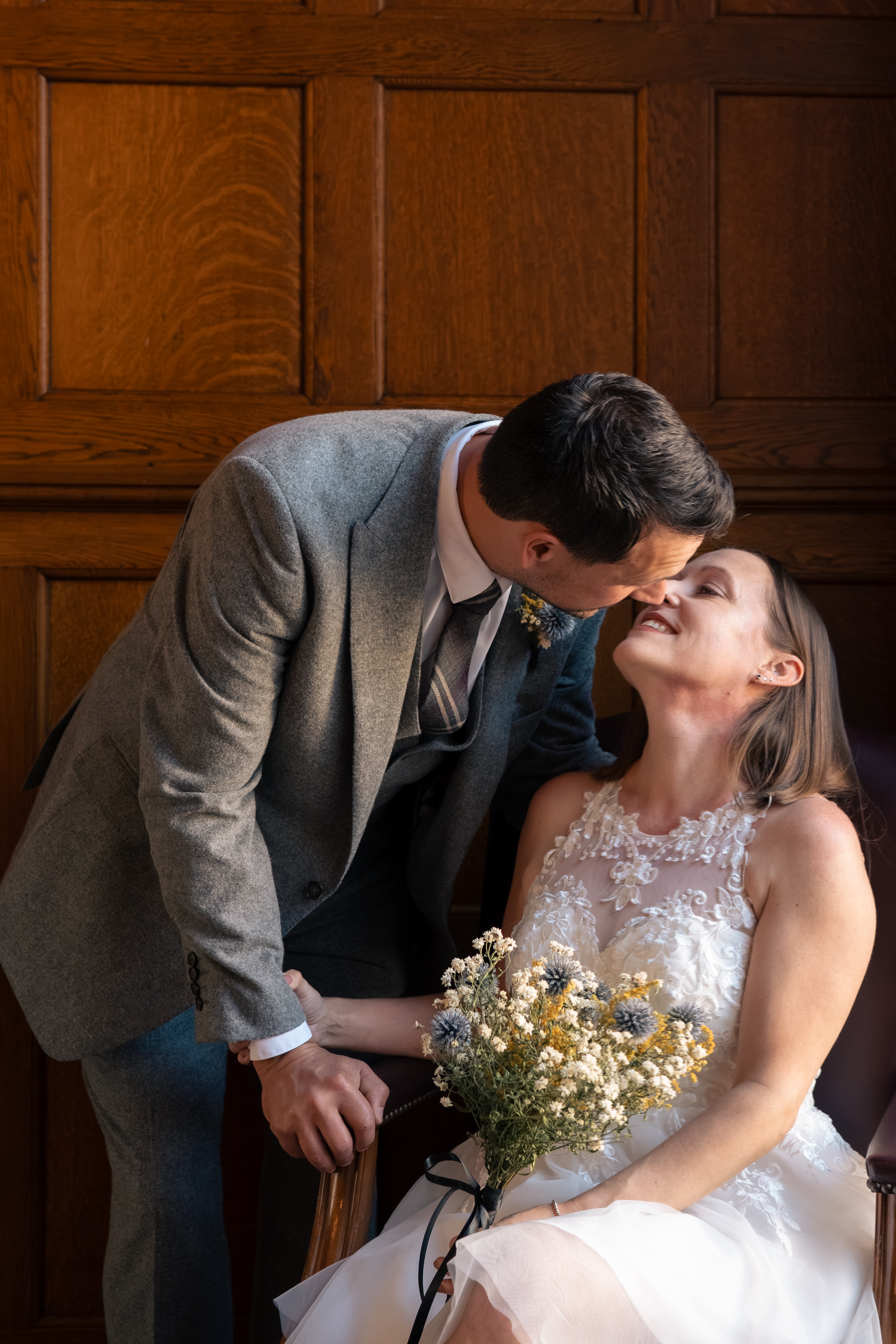 Bride in short white dress and groom in grey suit lean in for a kiss in Marischal College's Grant Room following their top secret Aberdeen elopement.