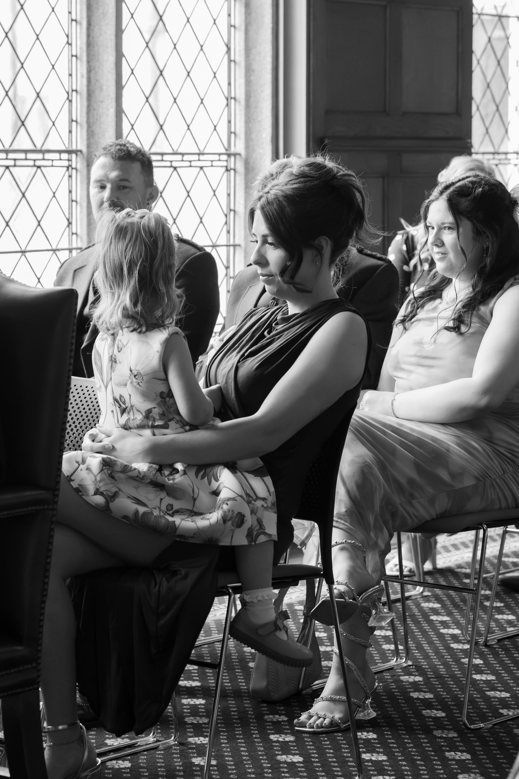 Aberdeen registry office wedding: Black and white photo of wedding guests. A child sits on her mother's lap, face turned away from the camera.