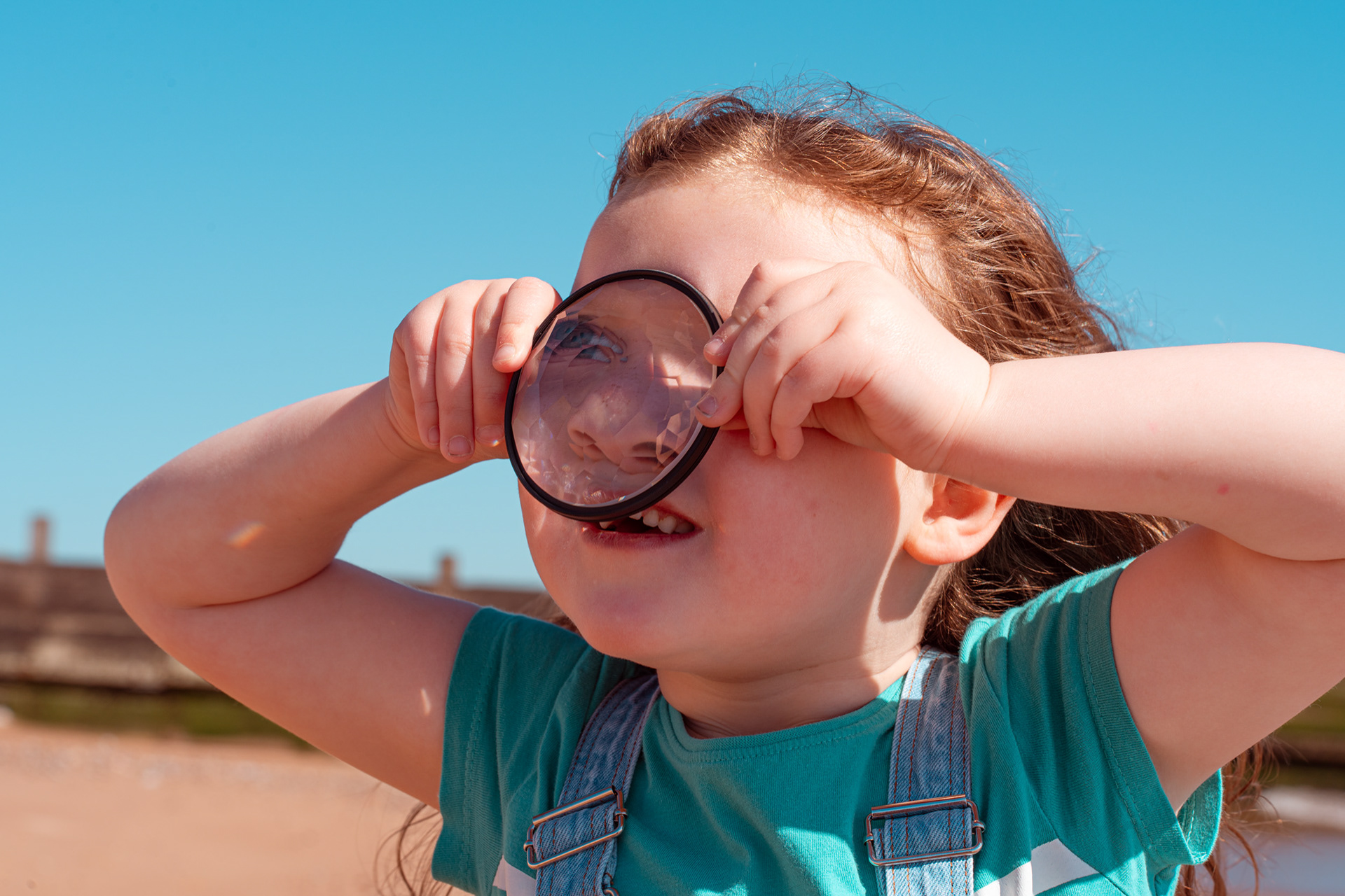 A little girl with white skin and long hair looks through a photographer's kaleidoscope filter, squishing it up against her nose, at an Aberdeen family photo session.