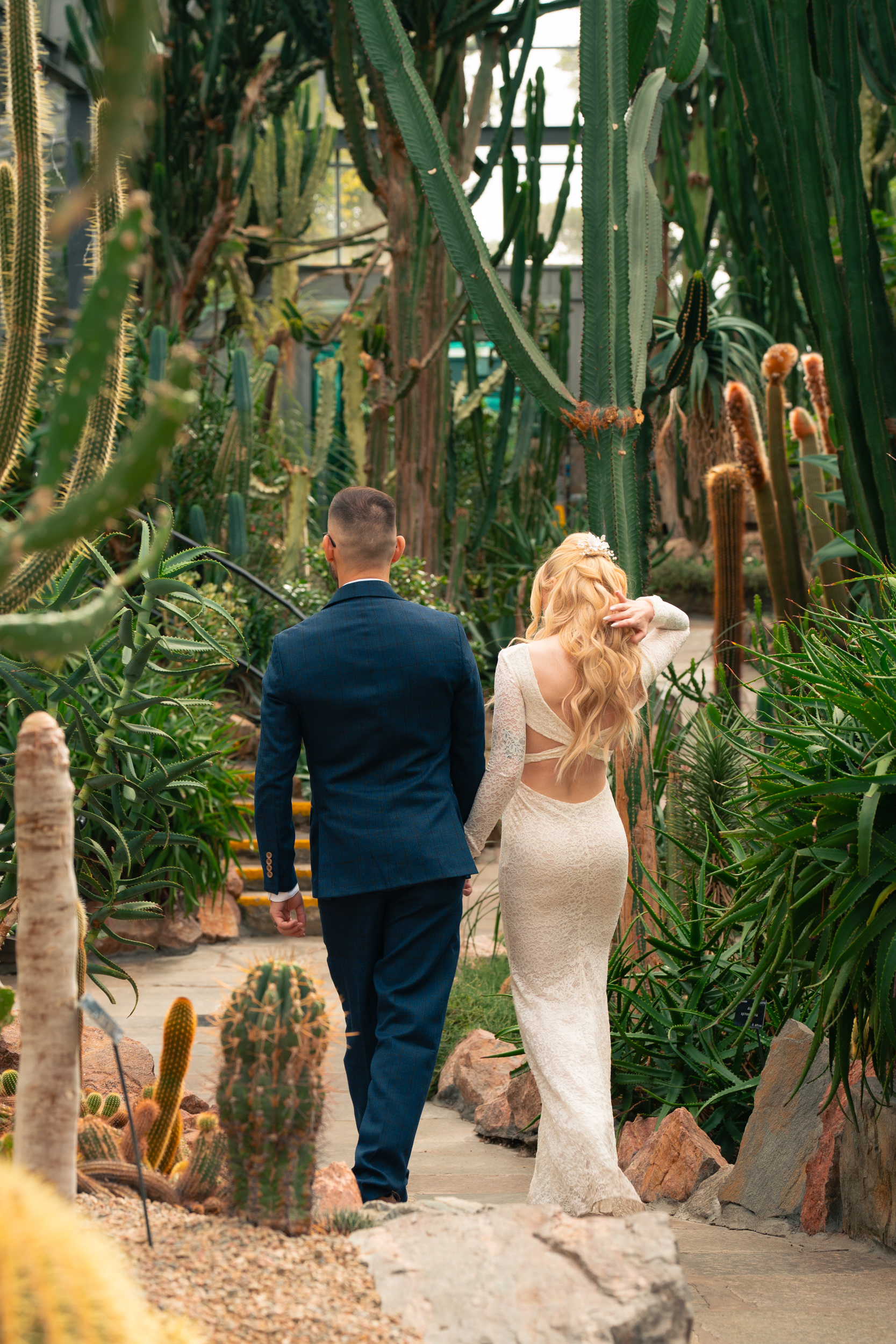 Duthie Park Winter Gardens wedding: Bride and groom walk hand in hand through the cactus house; she is playing with her hair.